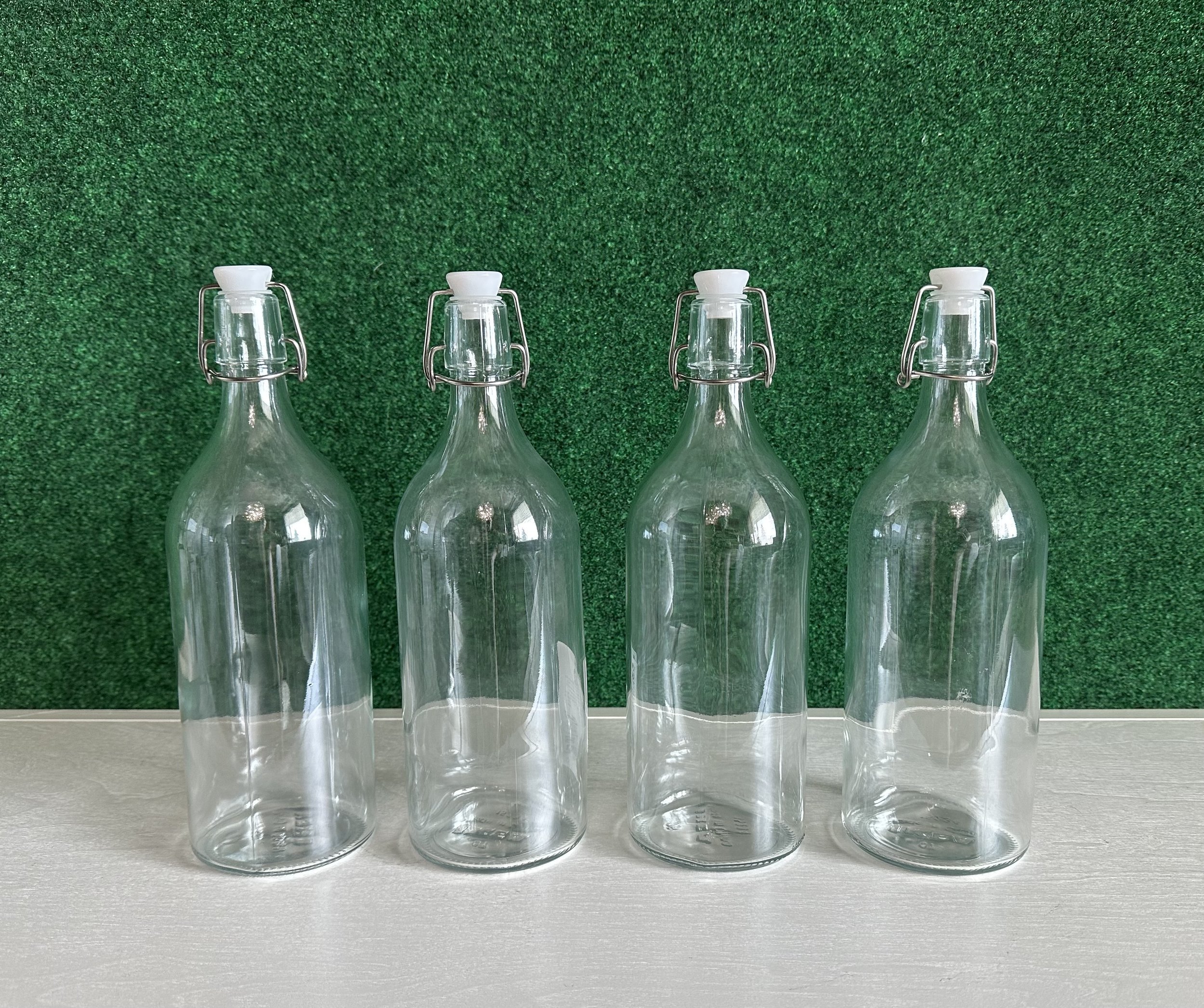 Four clear glass bottles with swing-top lids on a white surface against a green background.