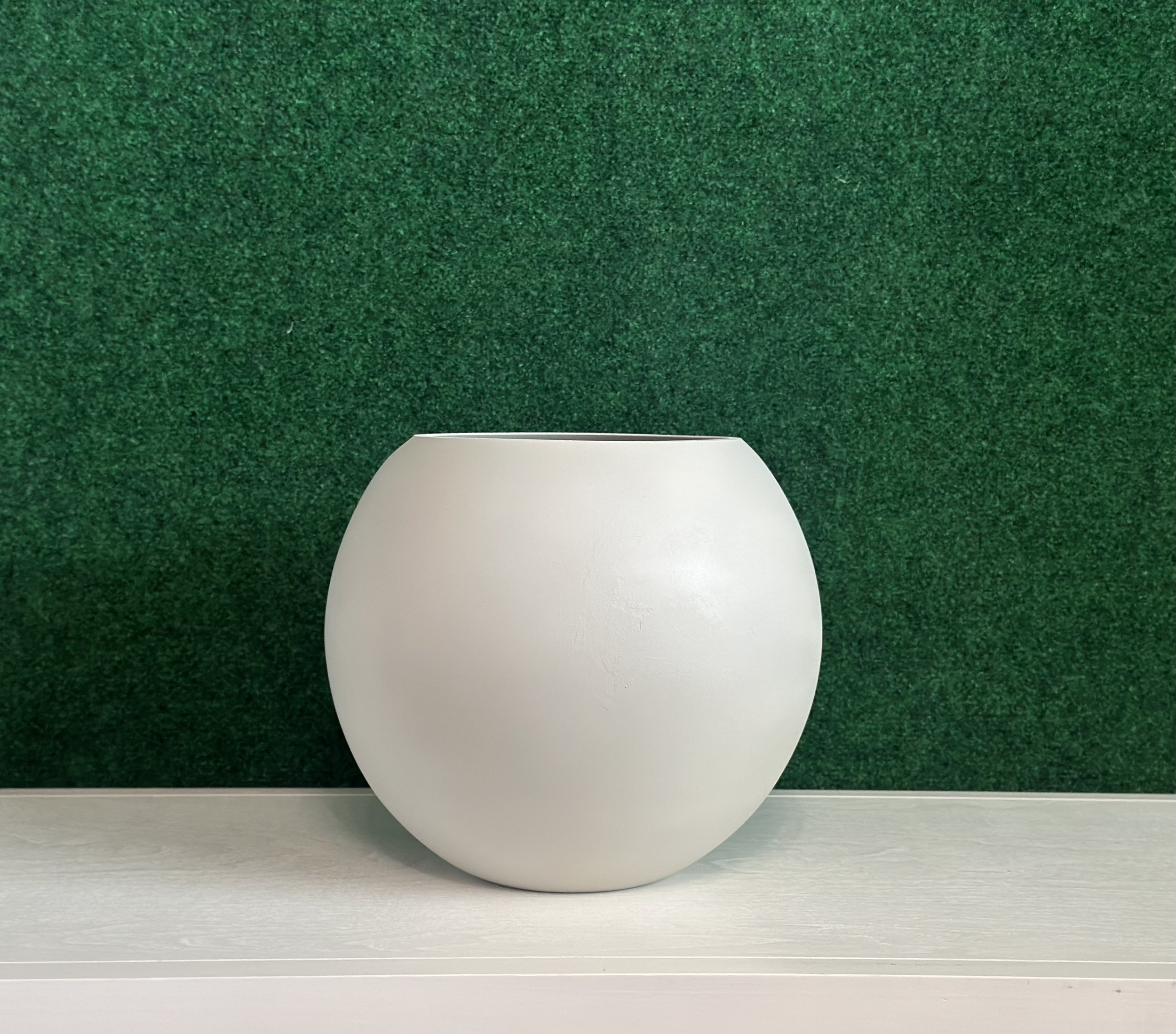 White spherical vase on a light surface with a green background.