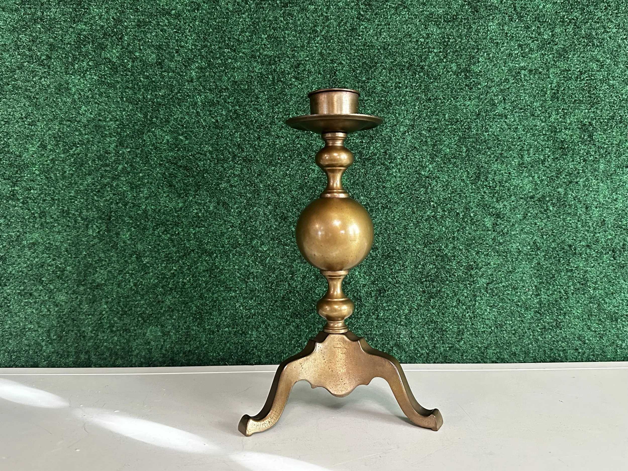 Vintage brass candlestick holder on a white surface with a green textured background.