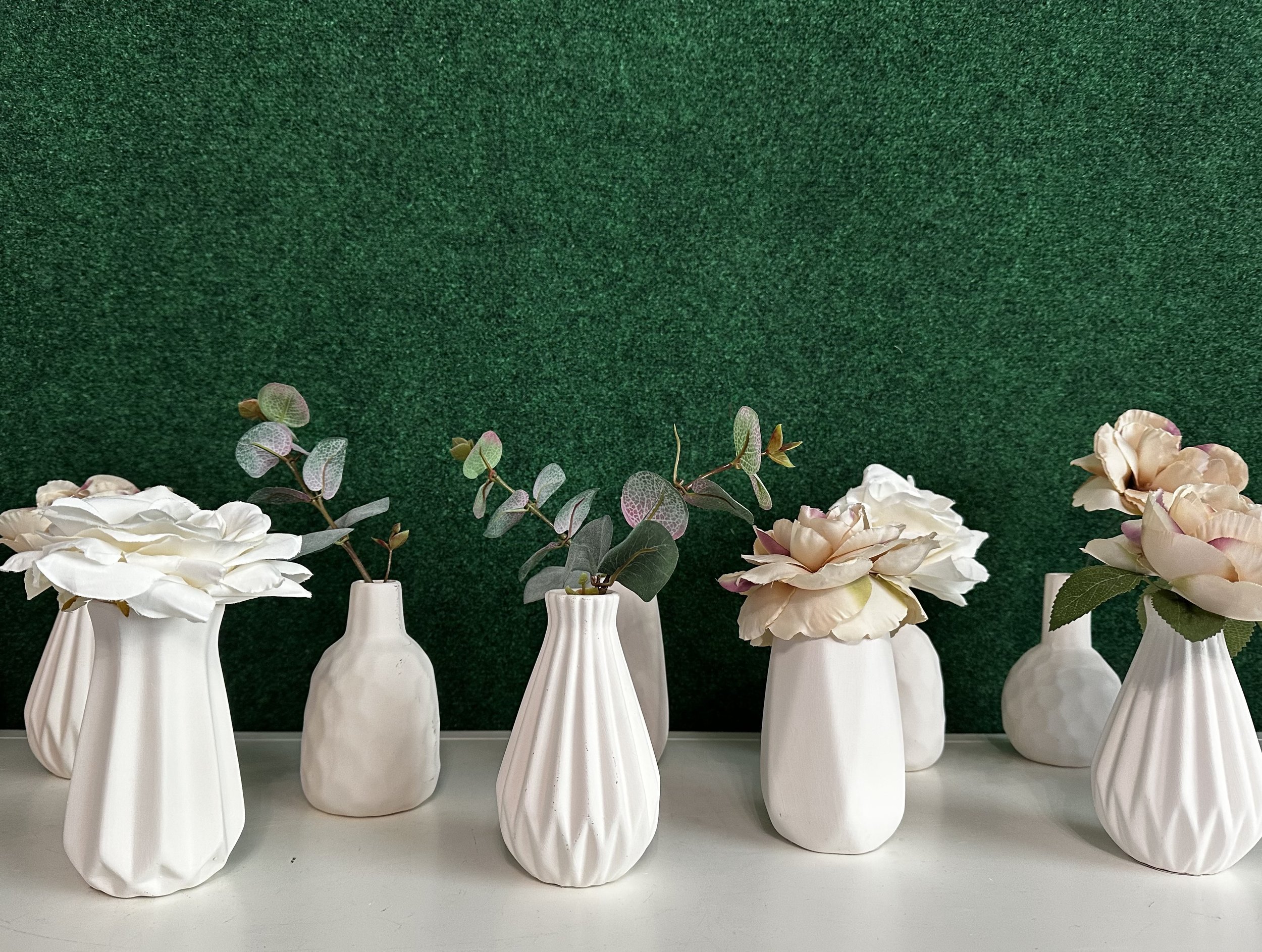 White ceramic vases with flowers and leaves, against a green background.