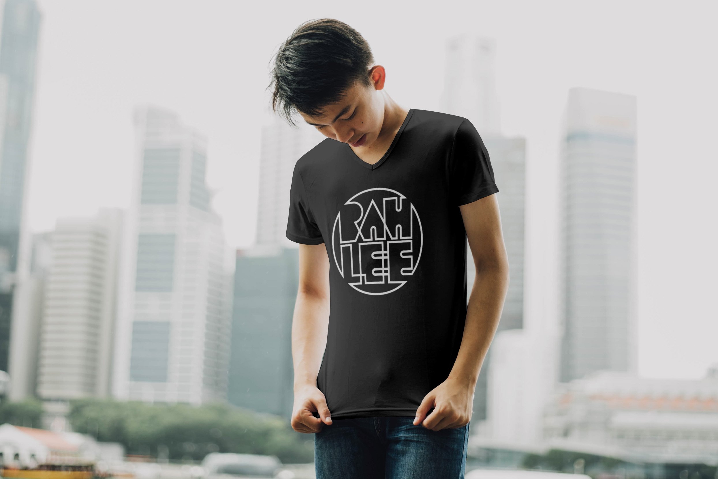 Rahlee outlined lettering in circle shape in white featured on gray shirt worn by man in from of city skyline