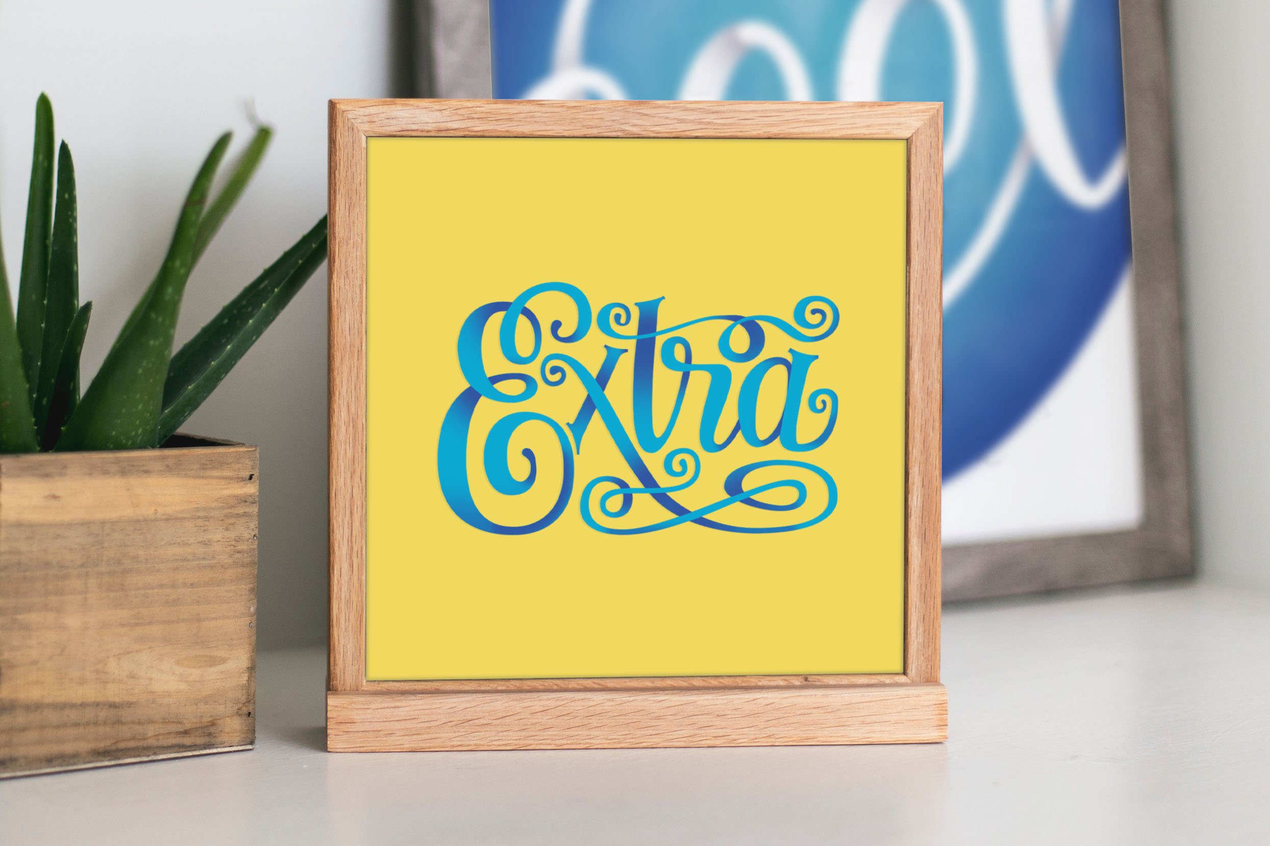 Blue and yellow Lettering print of the word "Extra" in a frame on a table.