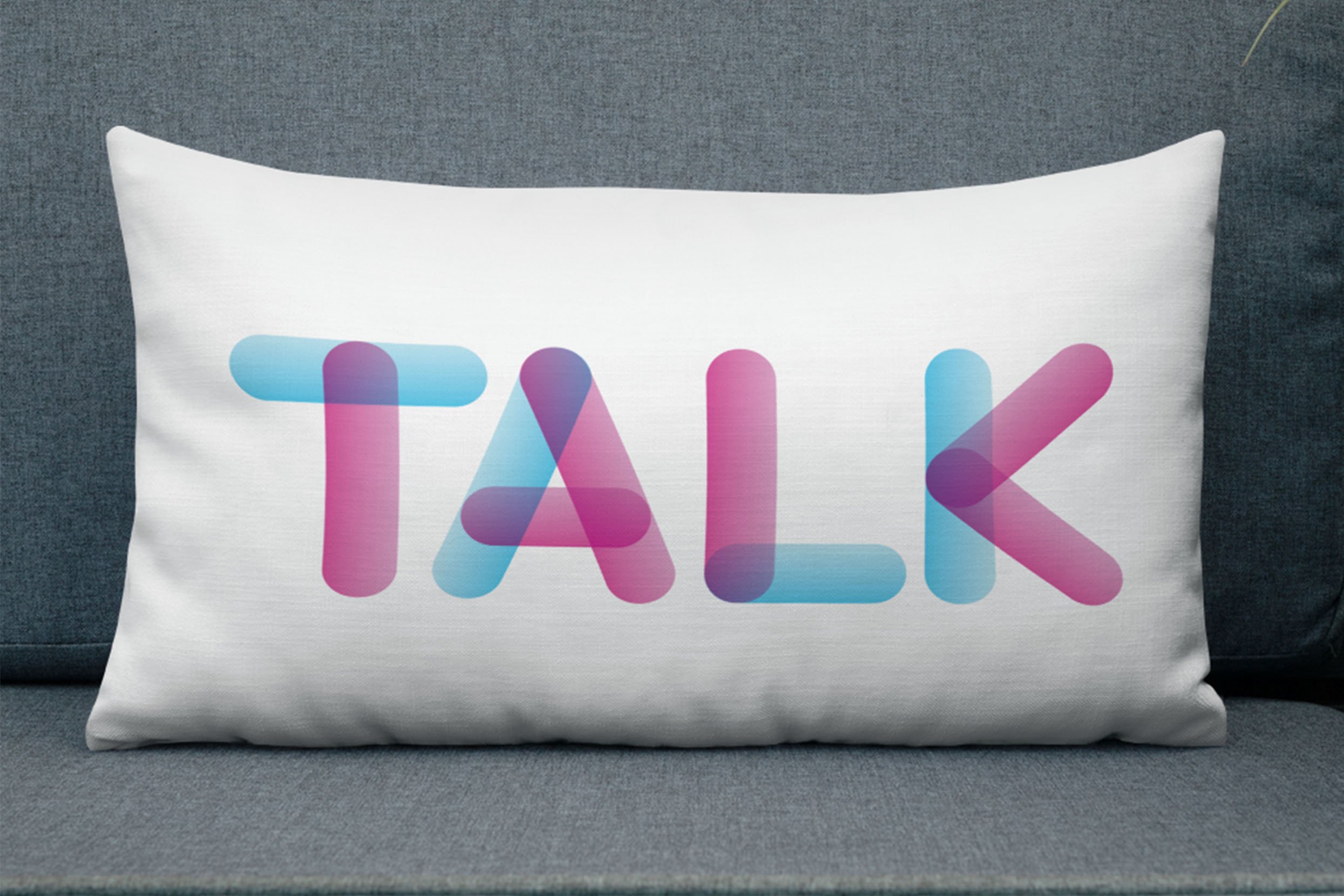 Pillow talk san serif all caps custom lettering in pink, blue and purple on white horizontal pillow on gray sofa