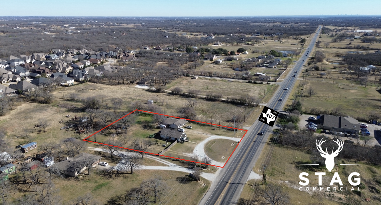 Aerial view of a residential area with a large empty lot outlined in red, including a house, cars, and trees. A major road runs parallel to the lot with a logo for Highway 407 and a stag head graphic at the bottom right corner.