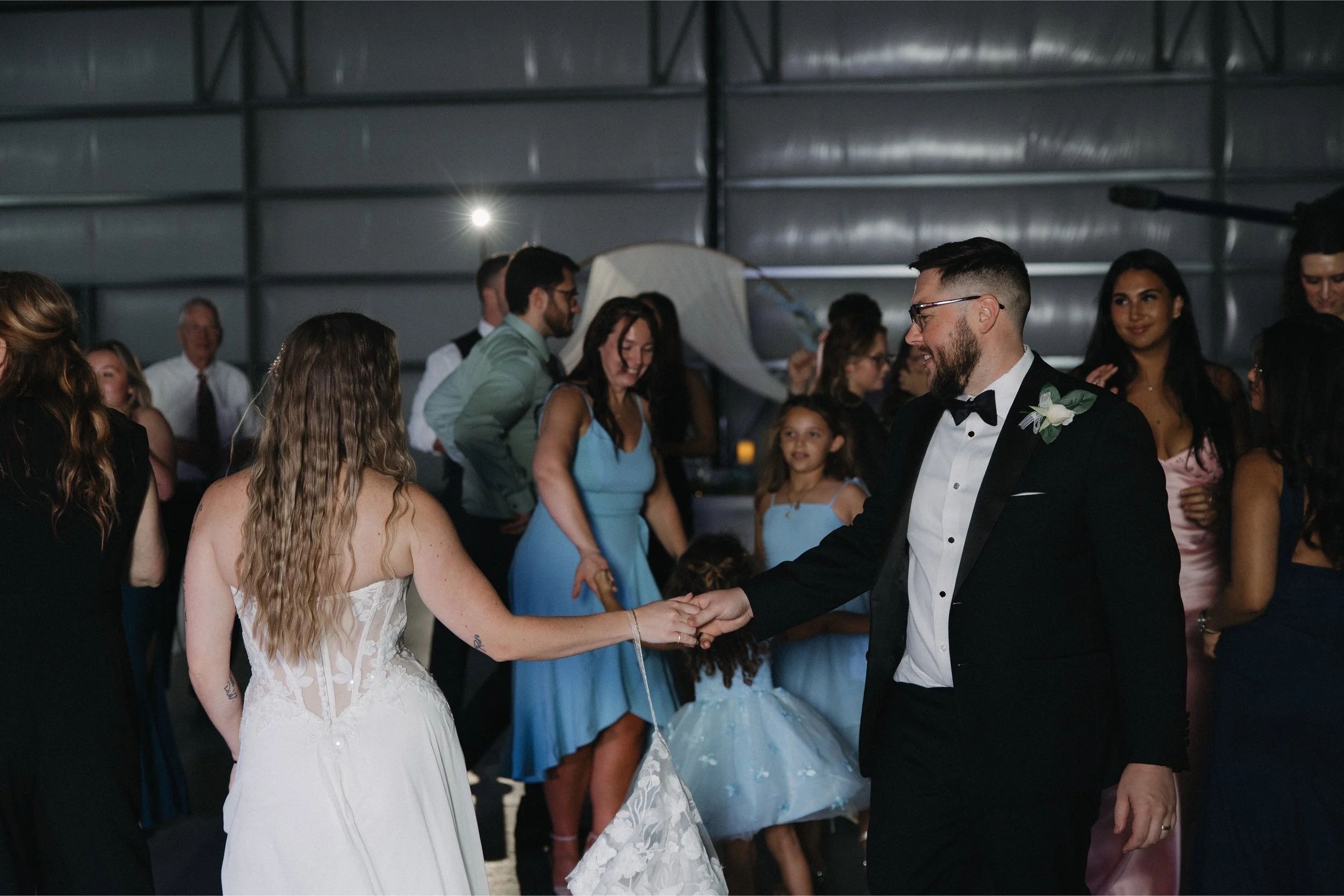 Couple dancing at a wedding reception with guests in the background inside a large industrial-style venue.
