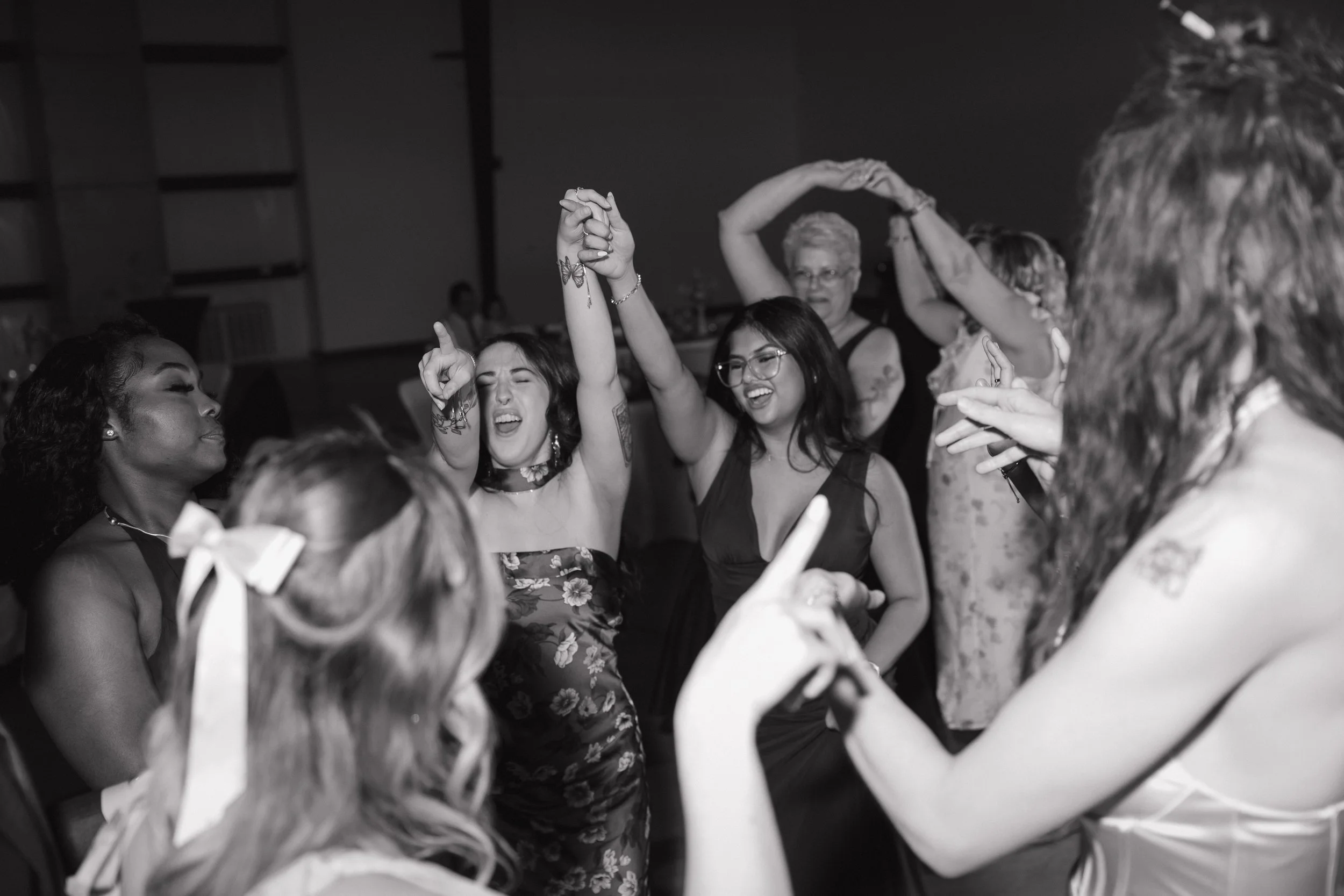 People dancing closely together at a social event, enjoying music and each other's company, with some holding hands or raising their arms.
