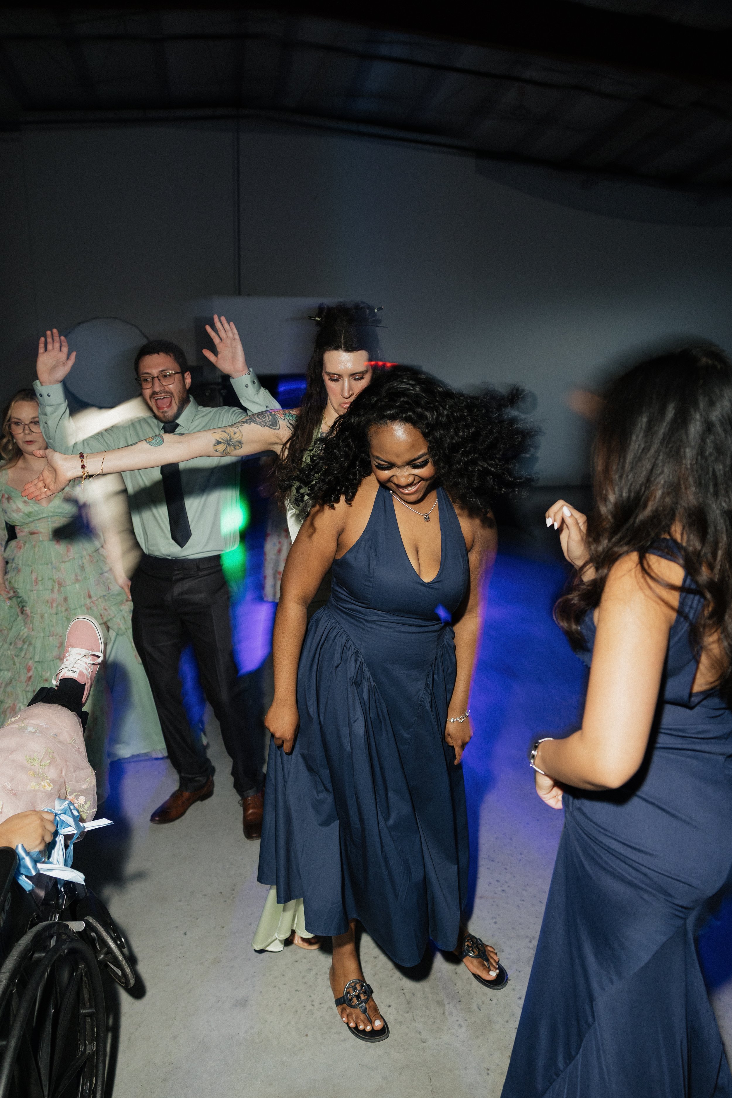 People dancing and celebrating at an indoor event, with one woman smiling and wearing a blue dress, while others around her are also enjoying themselves.