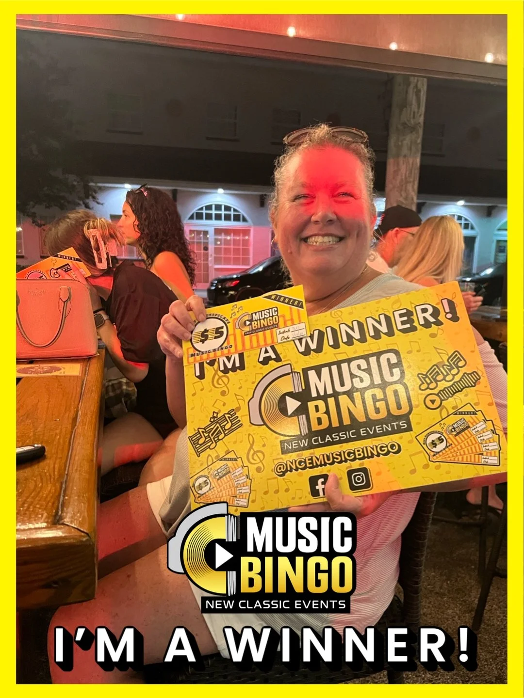 A woman smiling and holding a certificate and a sign that says she is a winner at Music Bingo, a music-themed event, in a lively indoor setting.
