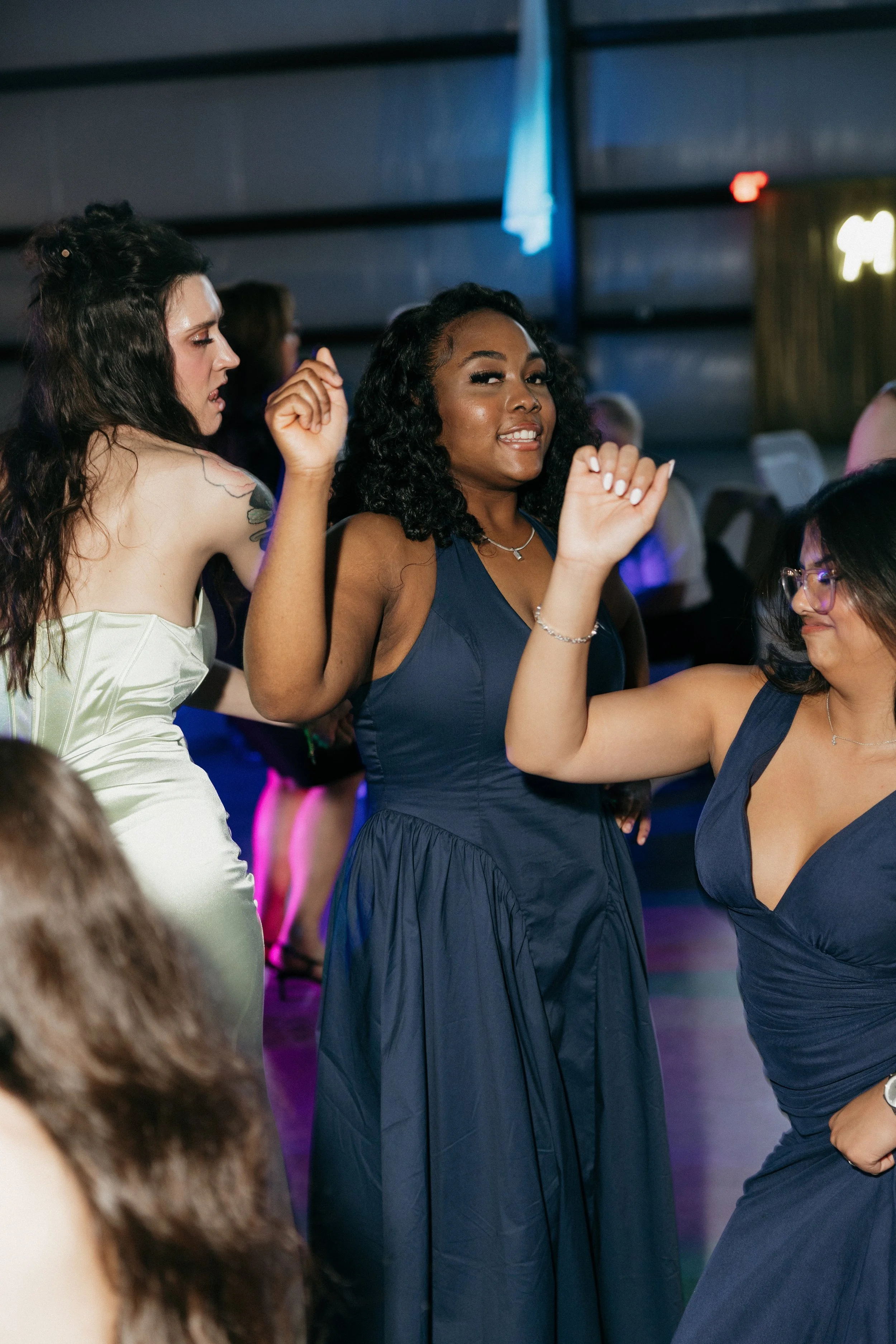 Group of women dancing and having fun at a social event or party, with colorful lighting in the background.