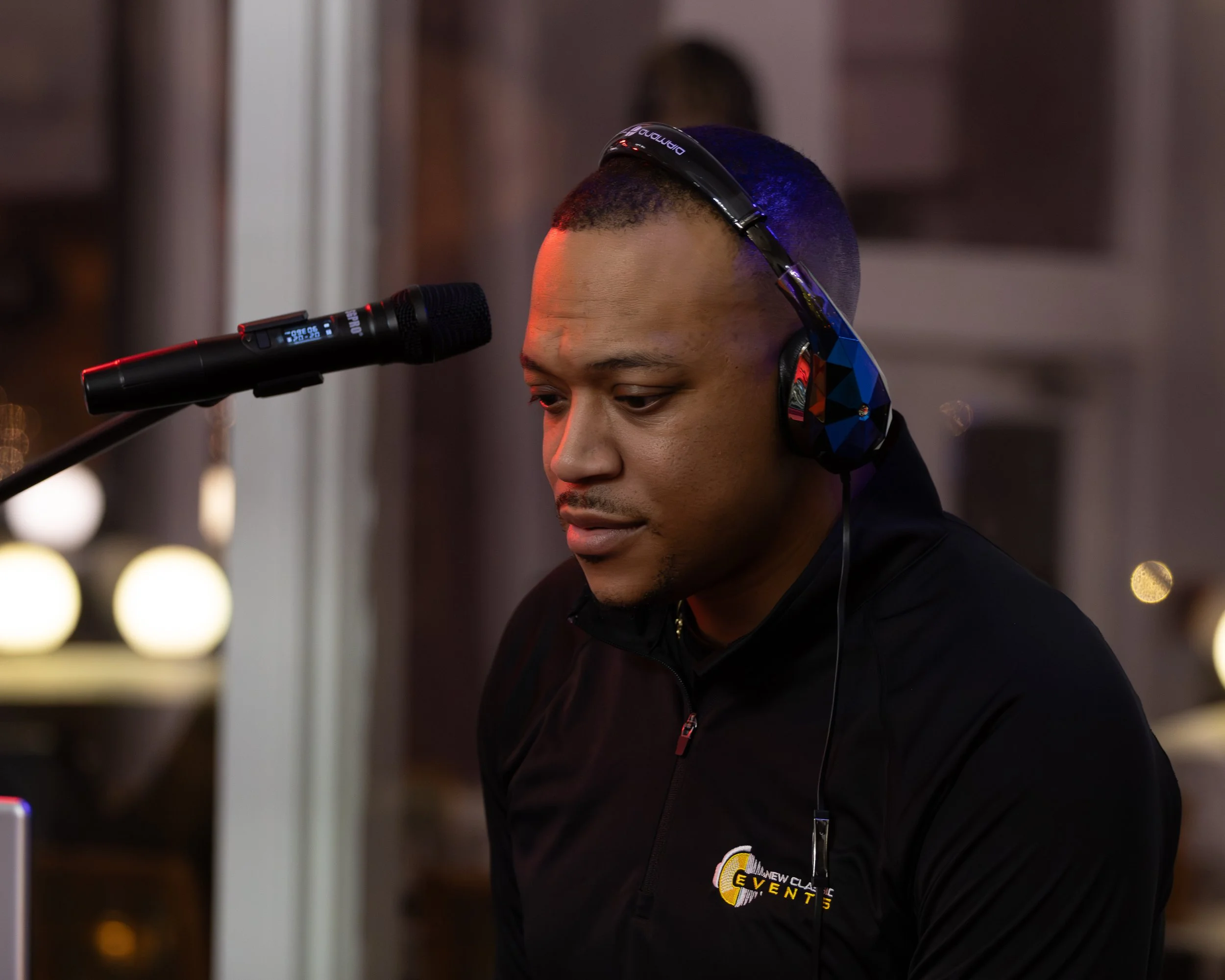 A man wearing headphones standing near a microphone indoors, looking down.