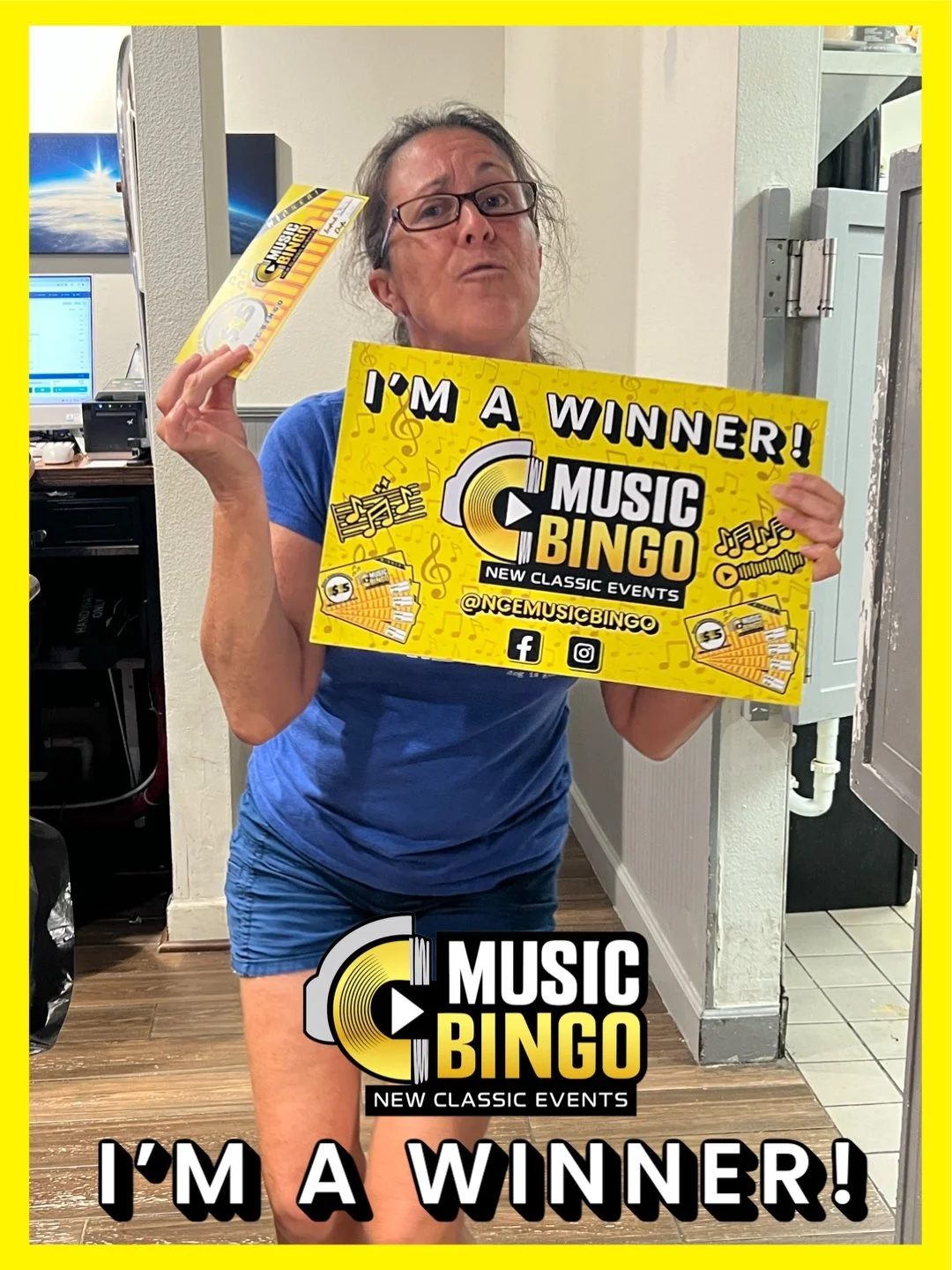 Woman holding a Billboard and a sticker, celebrating winning at Music Bingo. She is wearing glasses and a blue shirt, standing in a room with a computer and office supplies in the background.