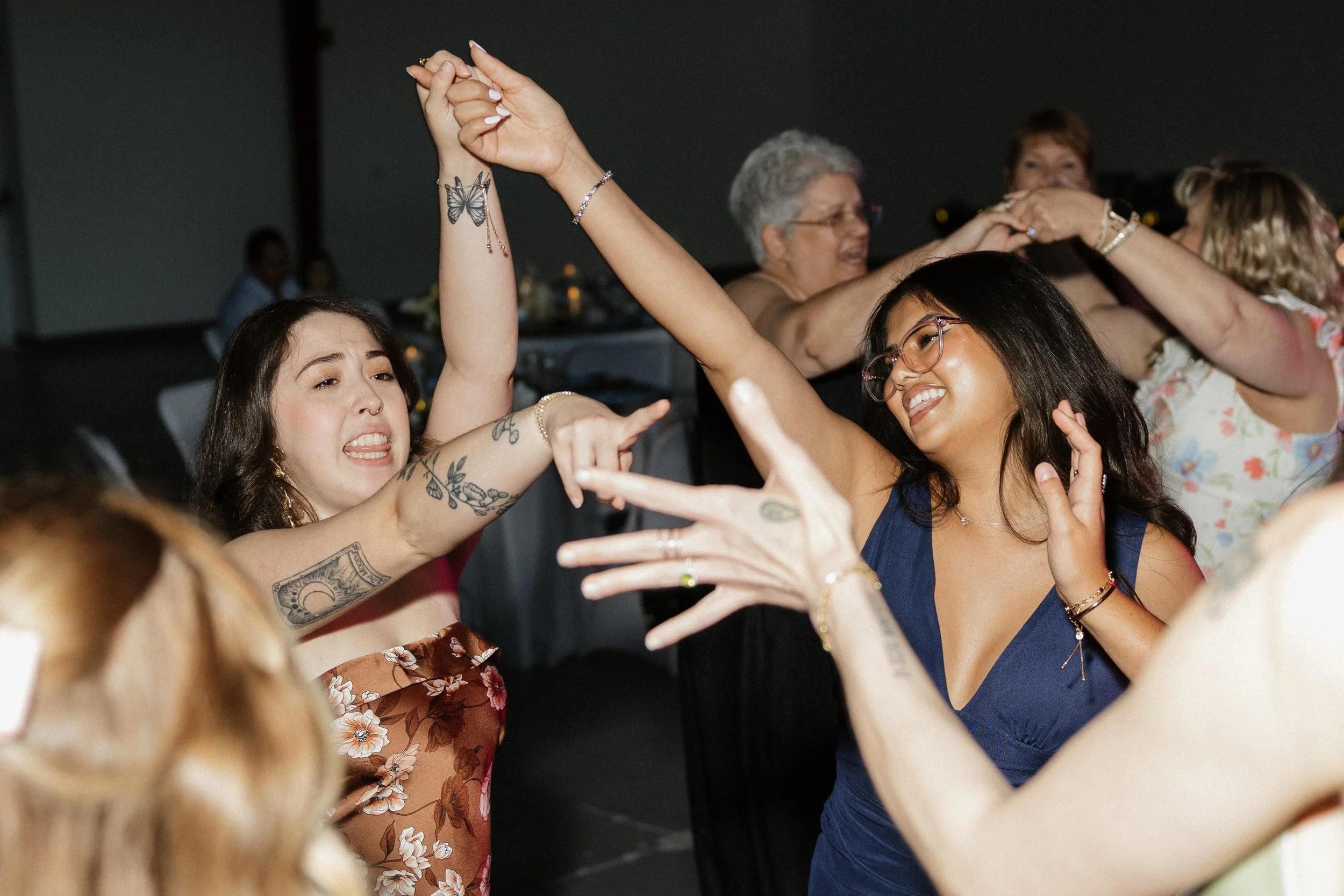 People dancing at a party, holding hands and smiling, with women wearing various dresses and accessories.