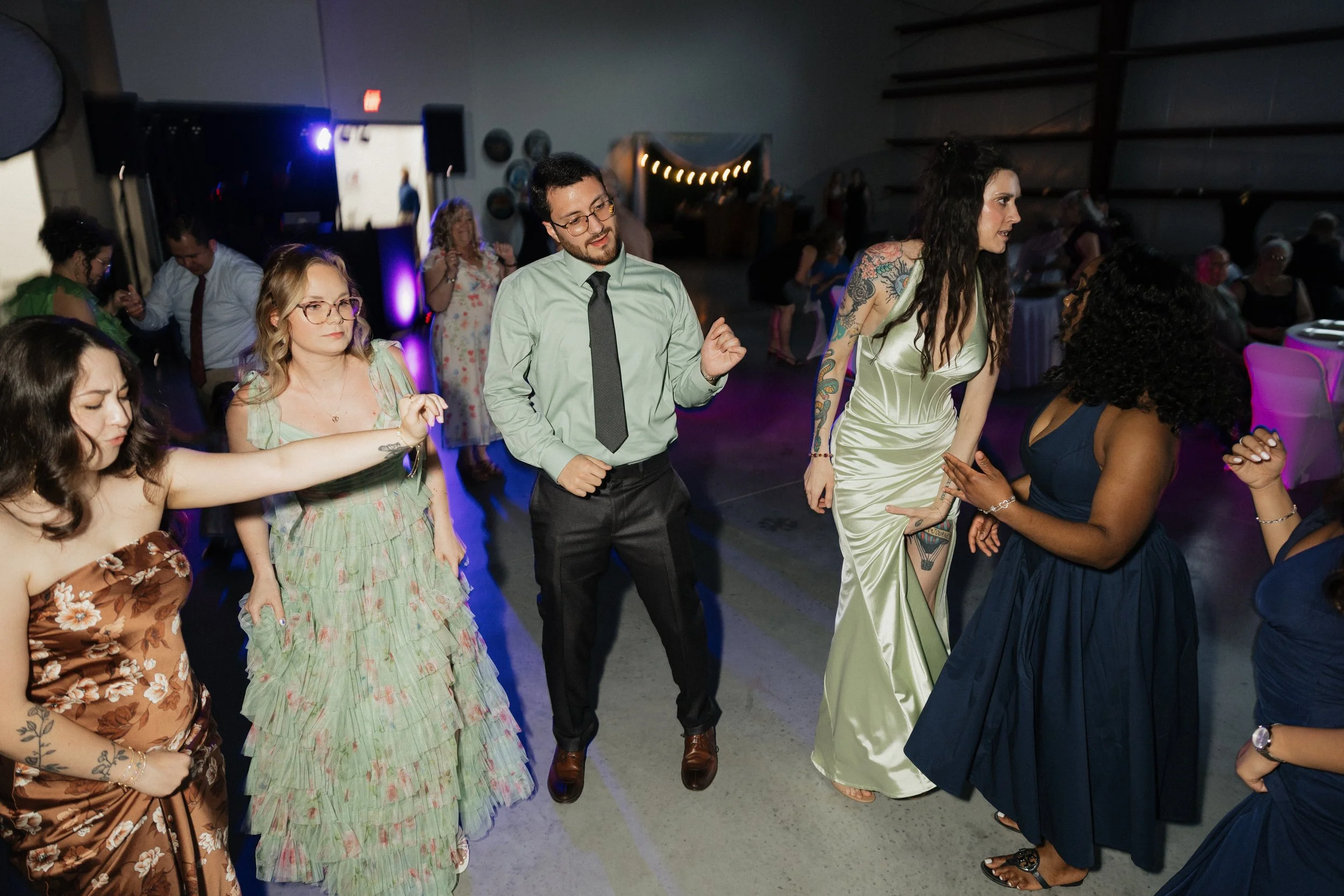 People dancing at a party or celebration indoors with dim lighting and purple accents.