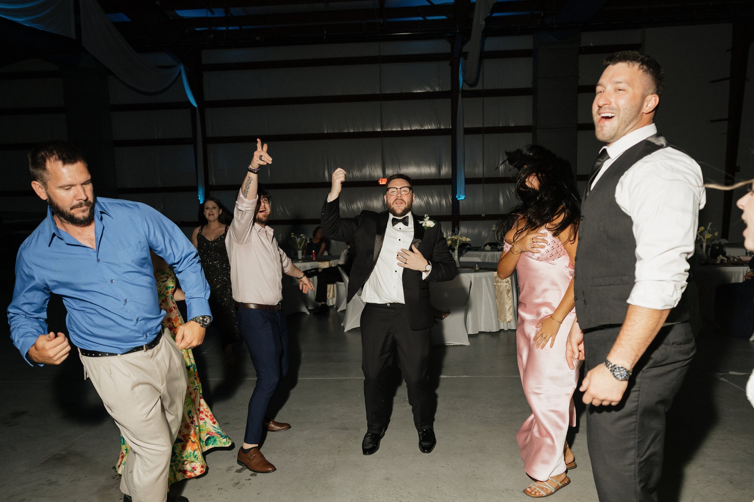 People dancing and having fun at a celebration or party in a large indoor venue, with some wearing formal attire.