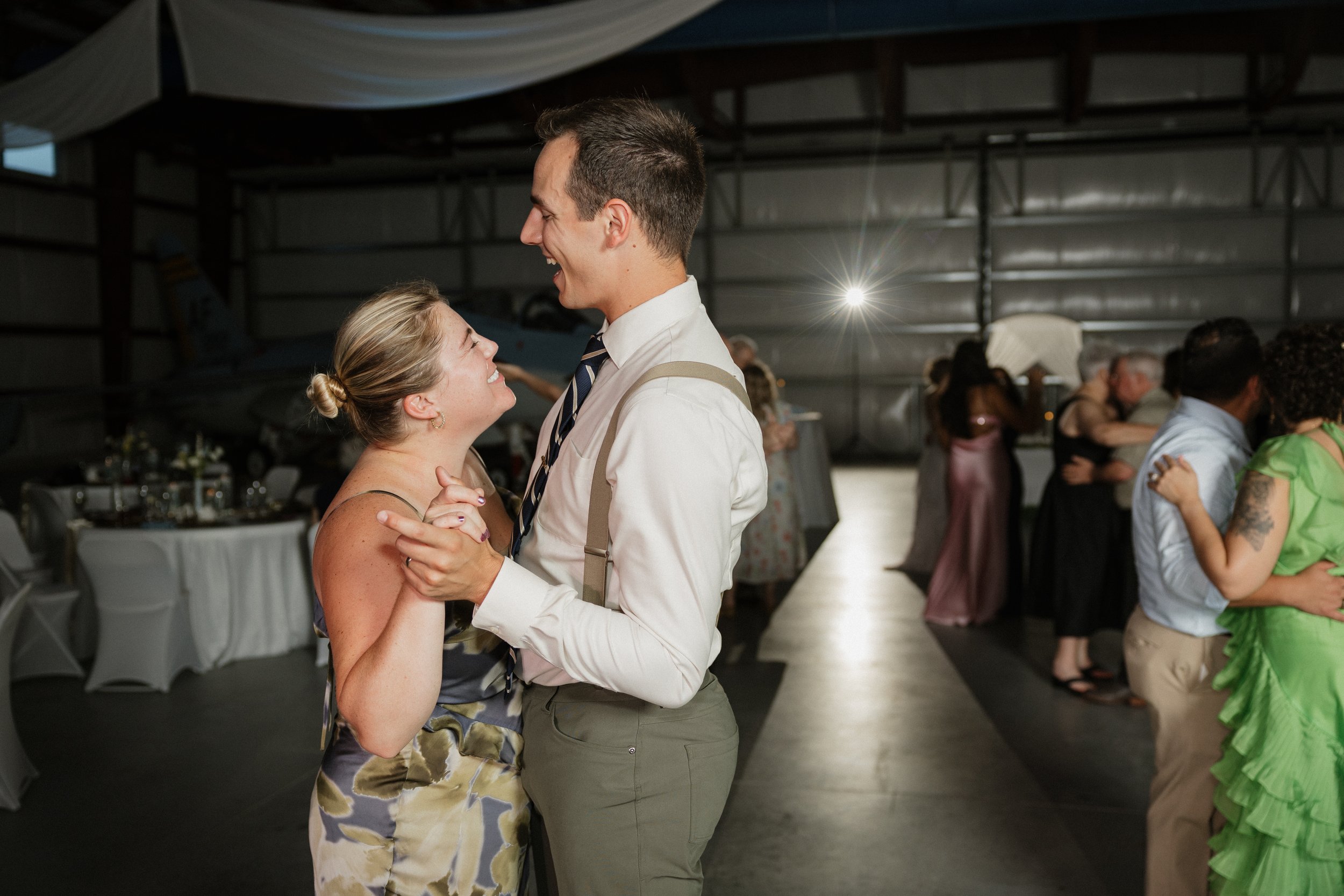 A couple sharing a dance at a social event or wedding reception in a large indoor venue, with other dancers and tables in the background.