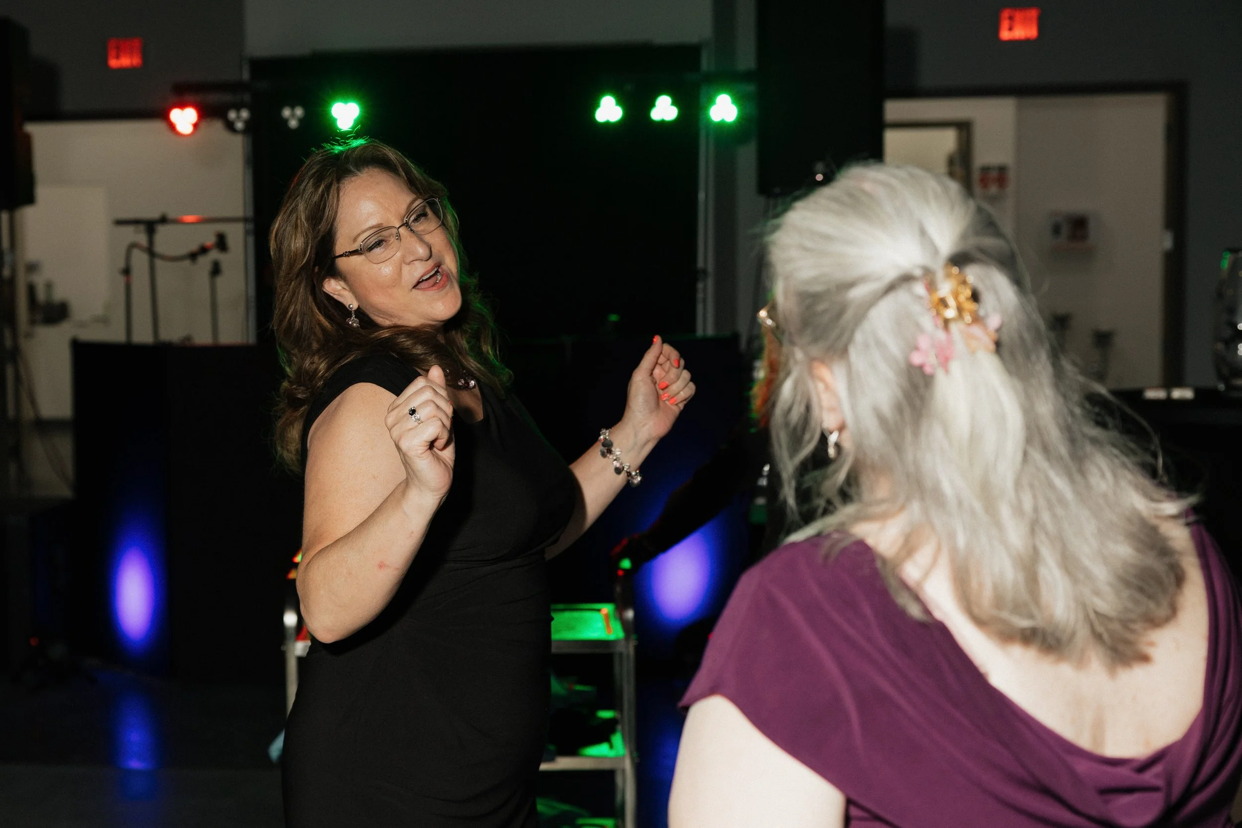 Two women dancing at a party with colorful lighting and a dark background.