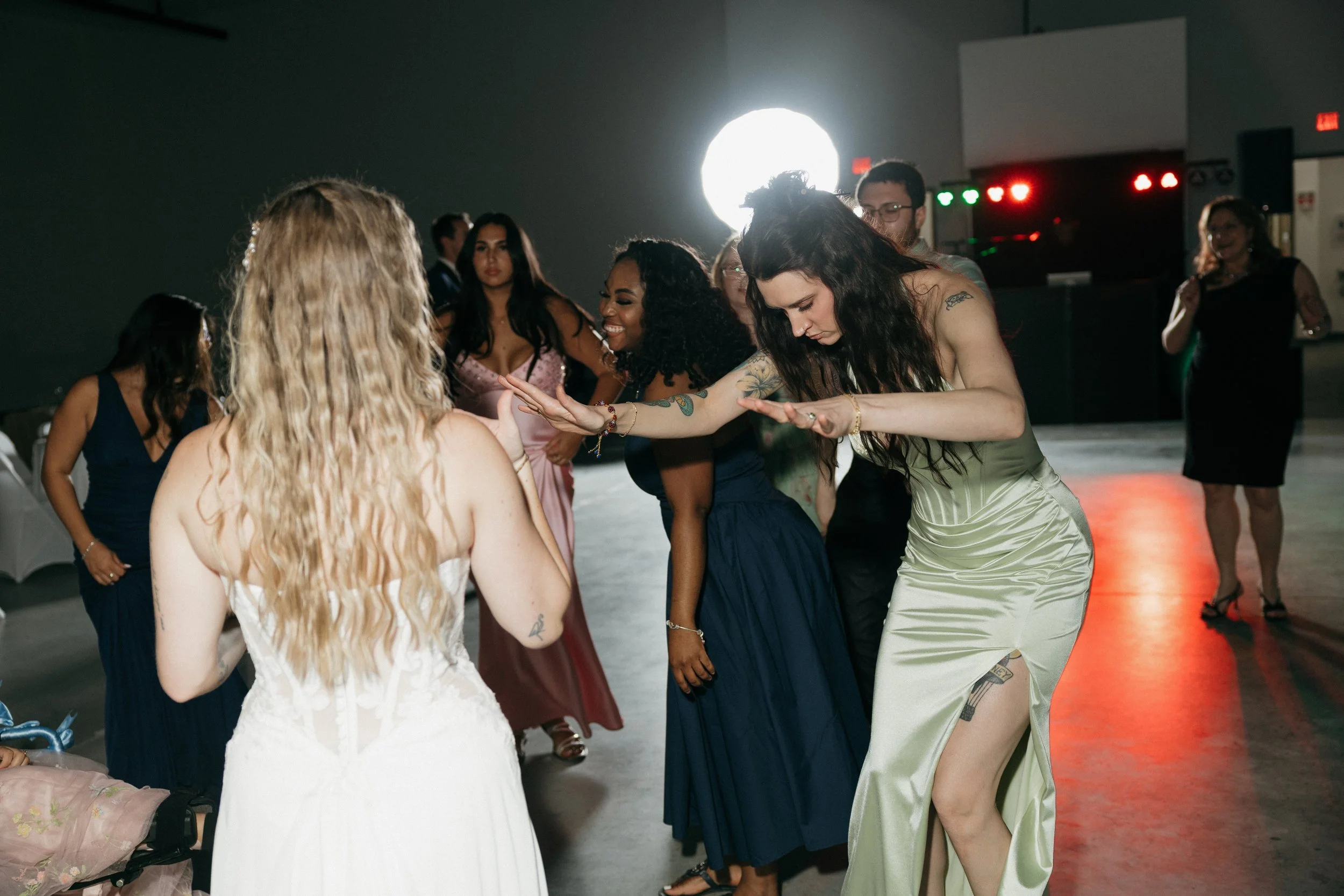 Group of women dancing and enjoying themselves at a party, with a DJ and colorful lighting in the background.