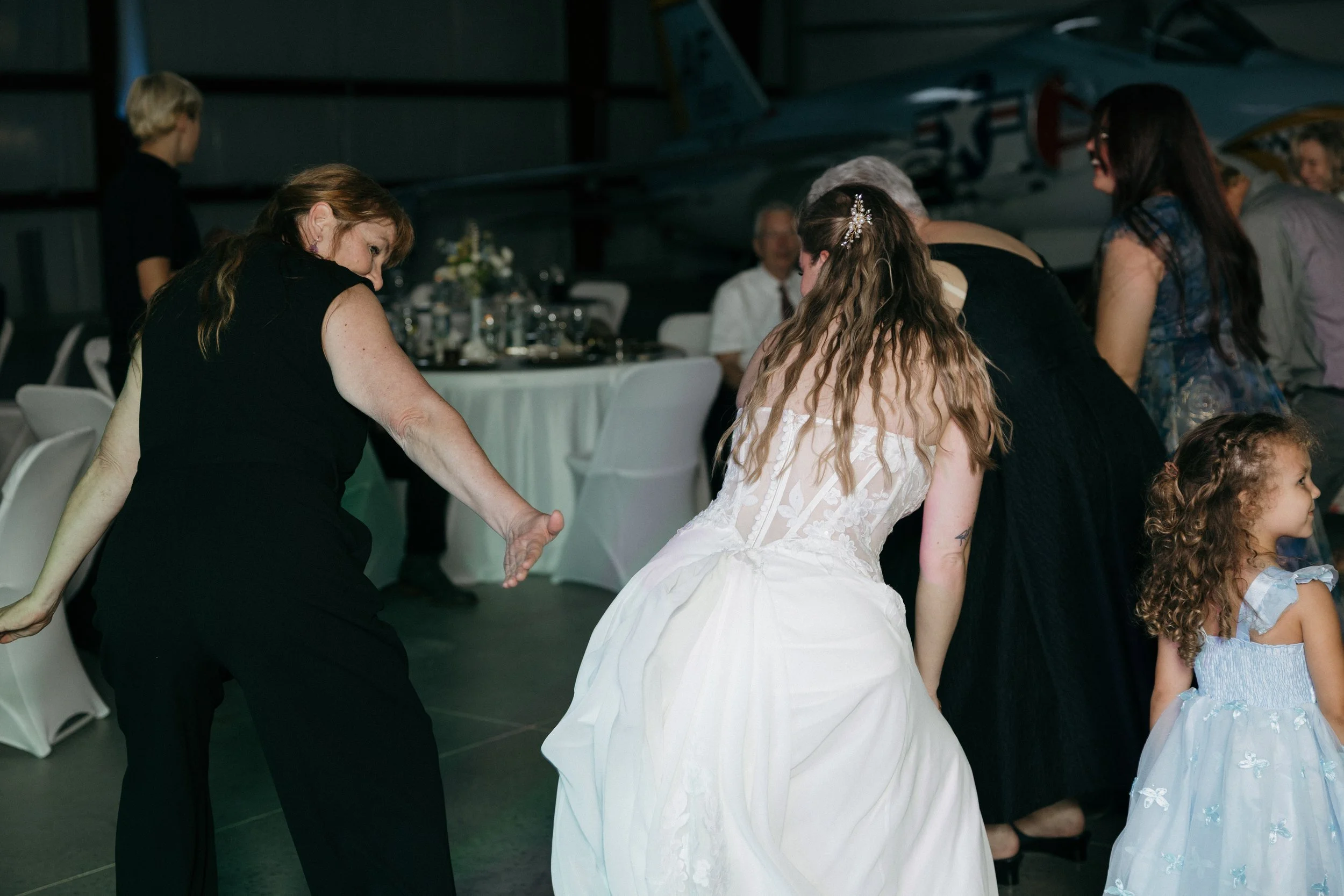 People dancing at a formal event in a hangar with a vintage aircraft in the background.