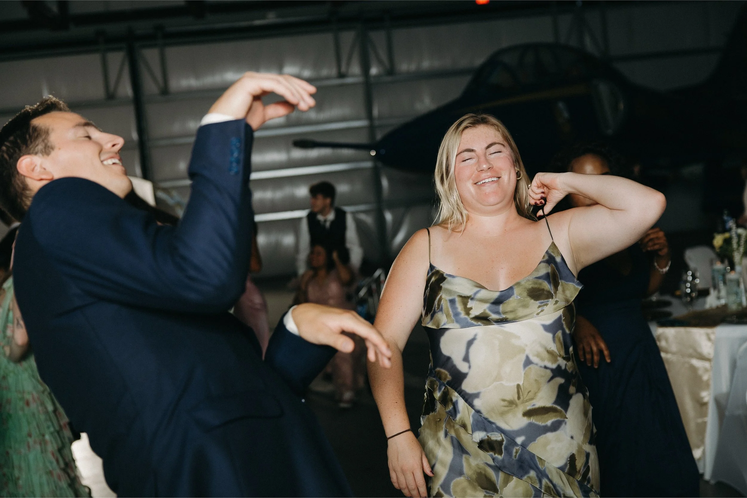 People dancing and socializing at a party in a venue with a black helicopter hanging from the ceiling.