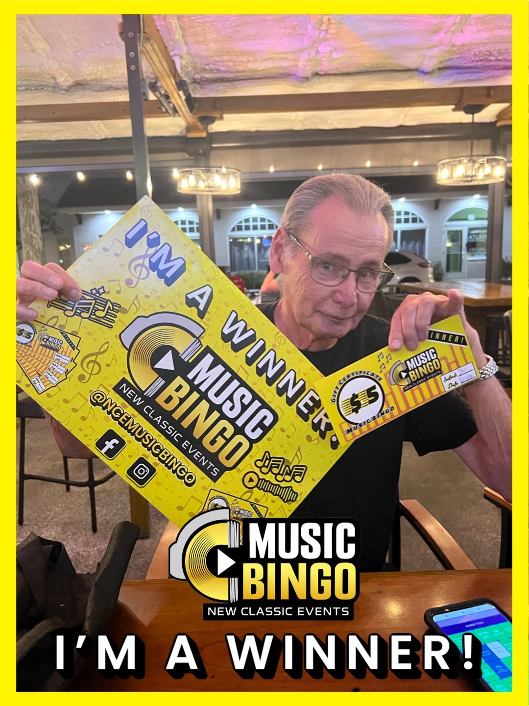 A man holding a yellow Music Bingo sign with the words 'I'm a winner!' at a restaurant or cafe.