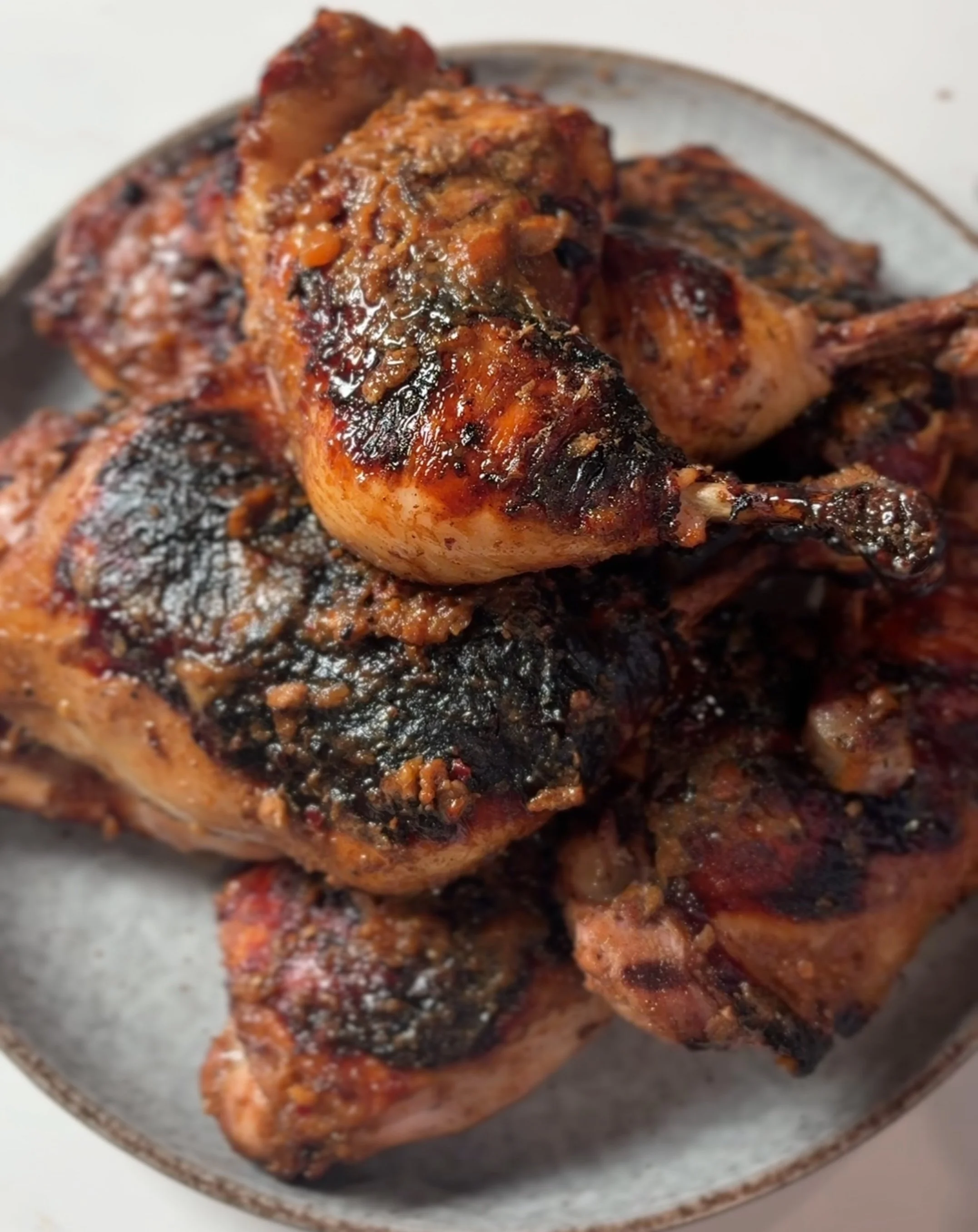 Close-up of cooked chicken pieces with a dark, spicy marinade or seasoning on a white plate.
