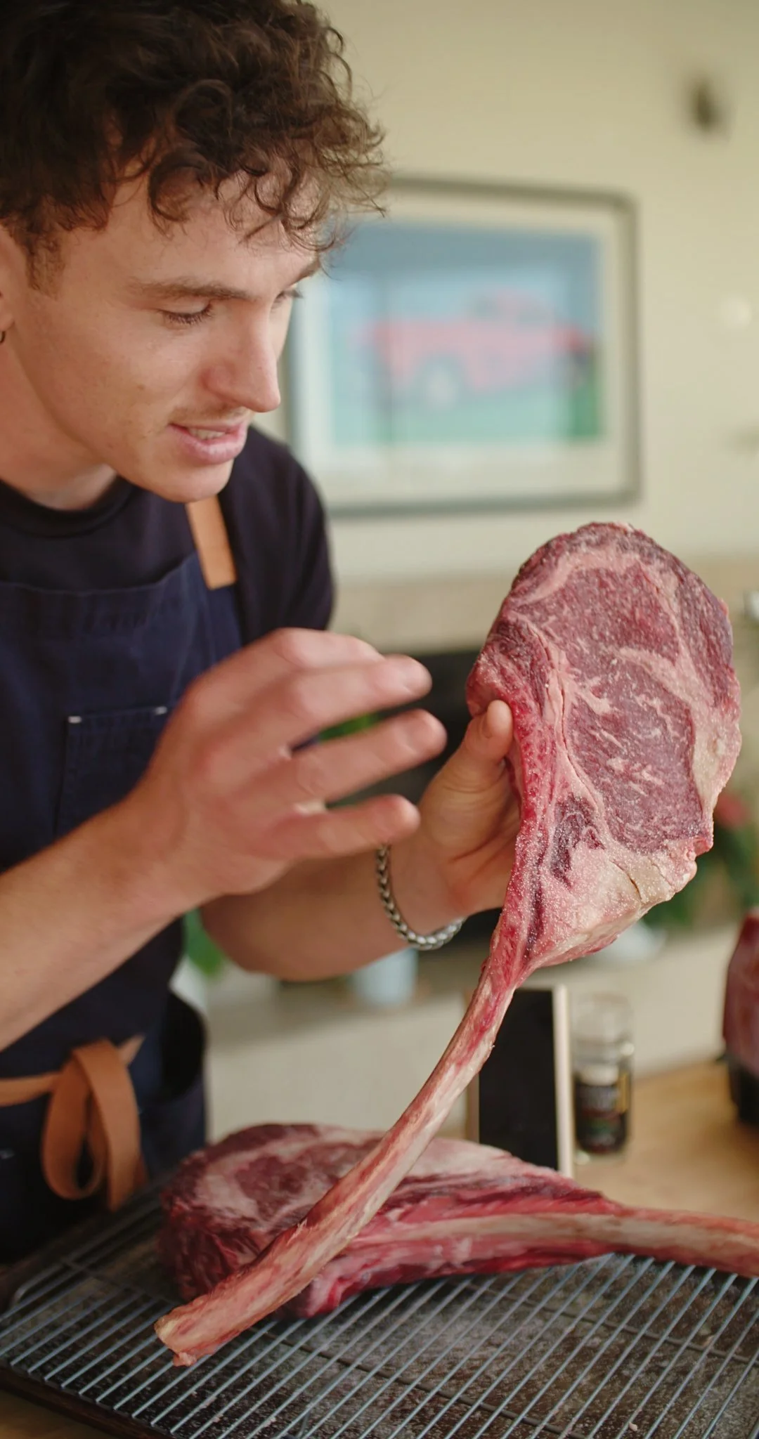 A person holding a large raw tomahawk steak with a long bone, preparing to cook it in a kitchen.