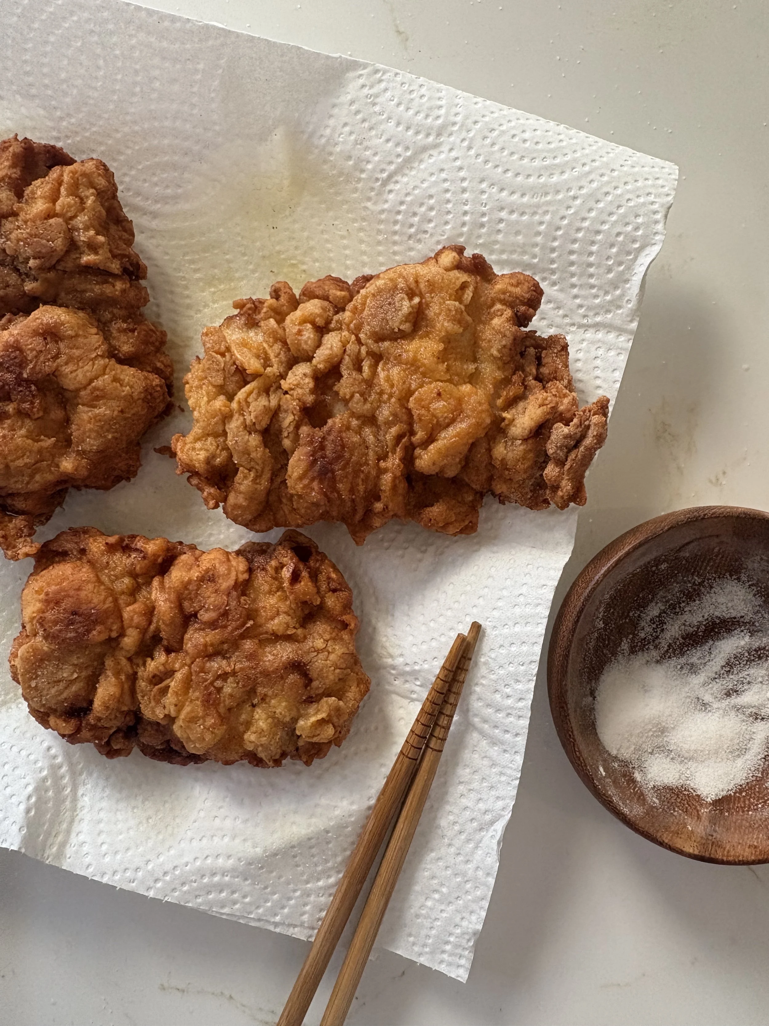 Fried chicken on paper towel with a small bowl of salt and chopsticks nearby.