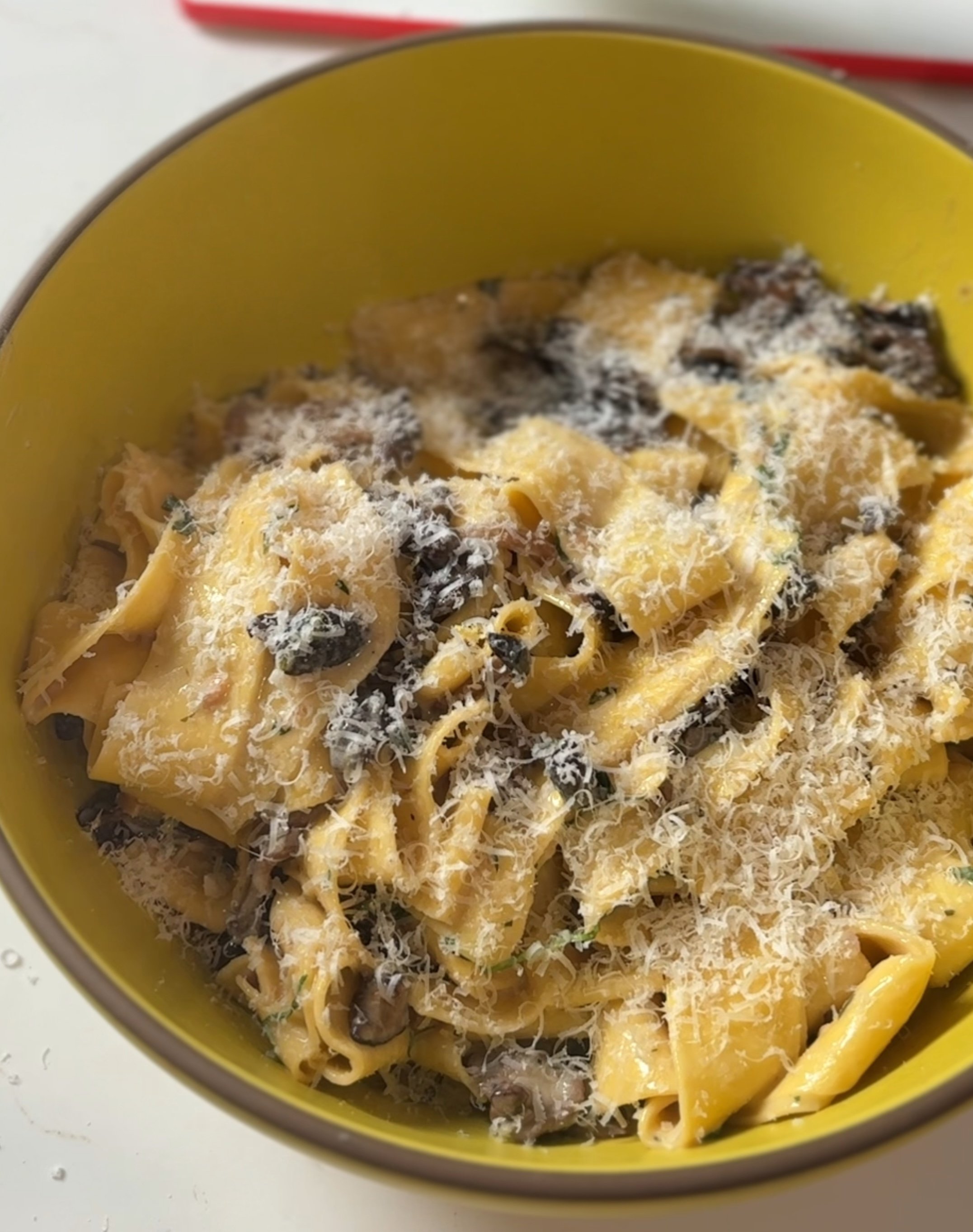 A bowl of cooked pasta with black mushrooms and grated cheese on top.