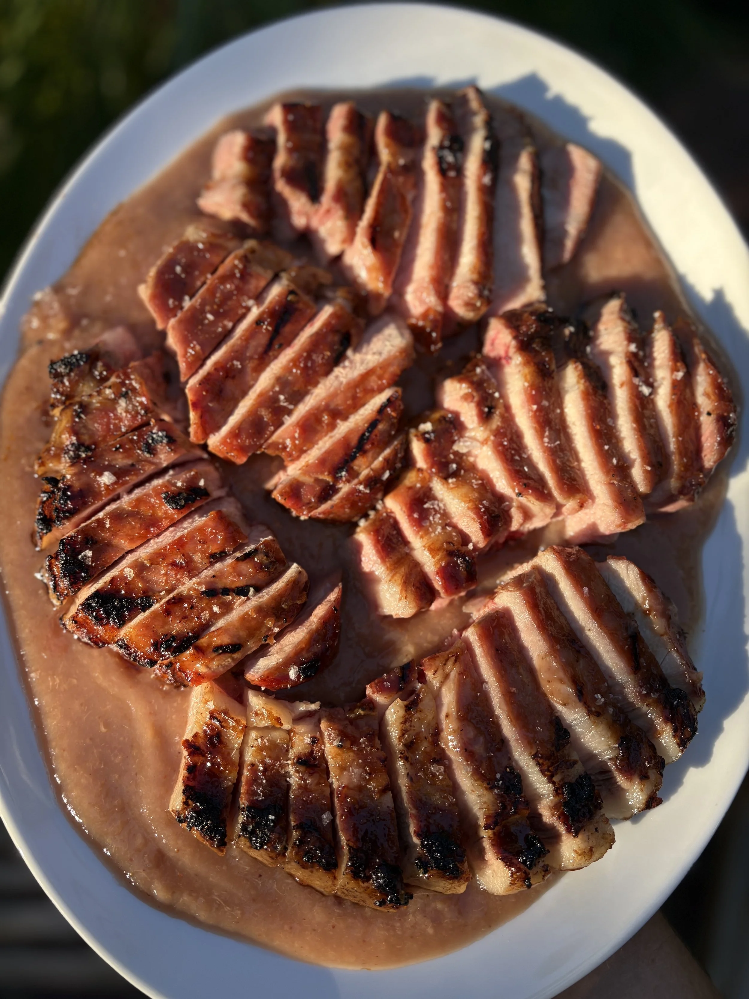 Grilled meat slices arranged on a plate with gravy or sauce.
