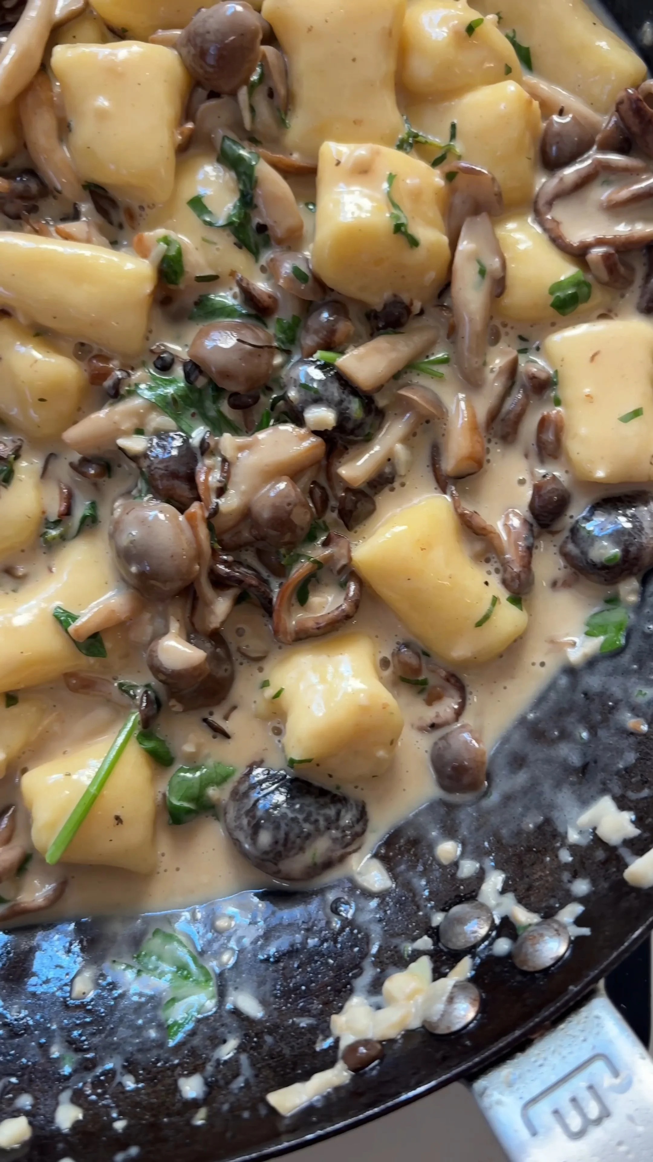 Creamy mushroom and potato dish with chopped herbs in a skillet.