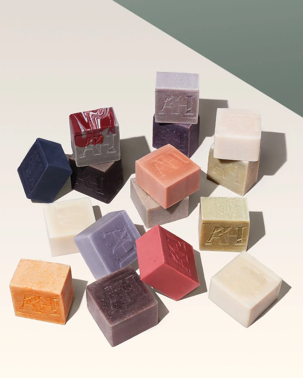 A collection of various colored soap bars with engraved initials or symbols, arranged on a white surface with shadows.