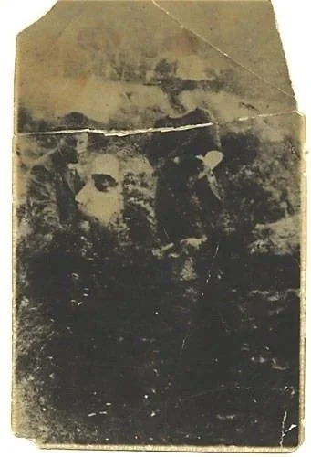 A faded old photograph that can be seen as a large bearded face or as a man holding a small child dressed in white