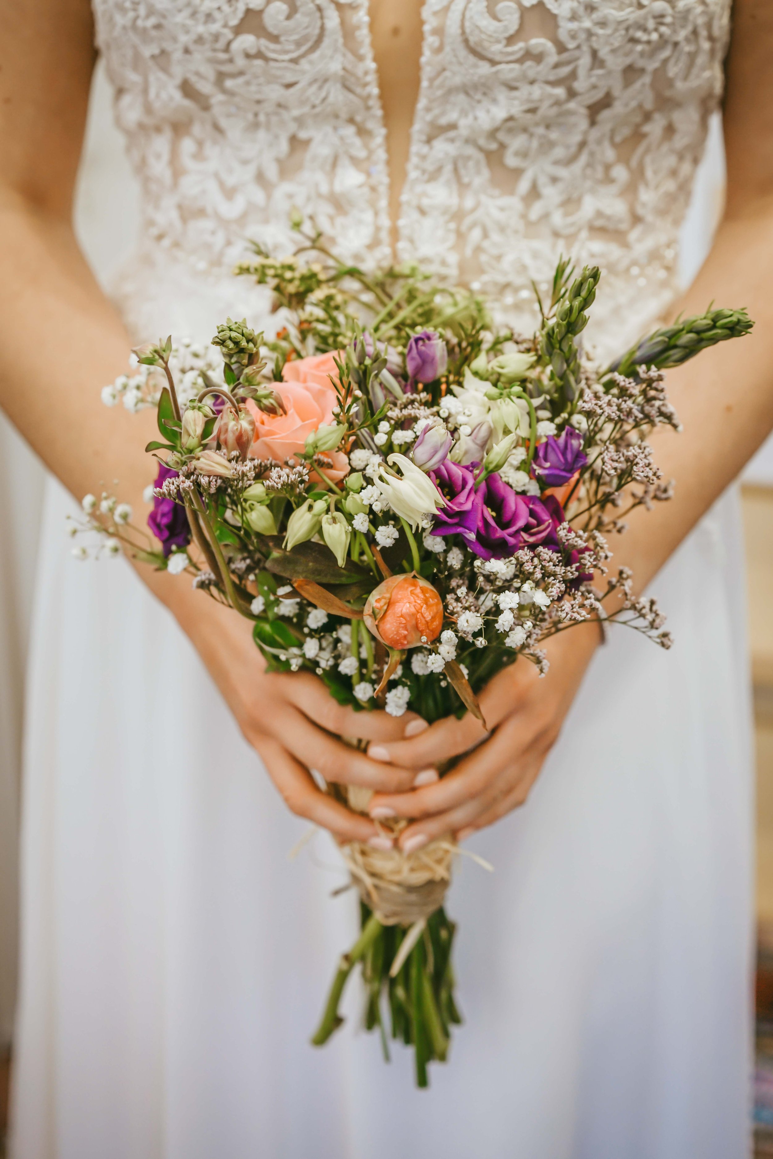 close-up-photograph-of-brides-flowers-held-in-both-hands-in-dress-featuring-fresh-lilac-peach-white-green-and-purple-varieties.jpg