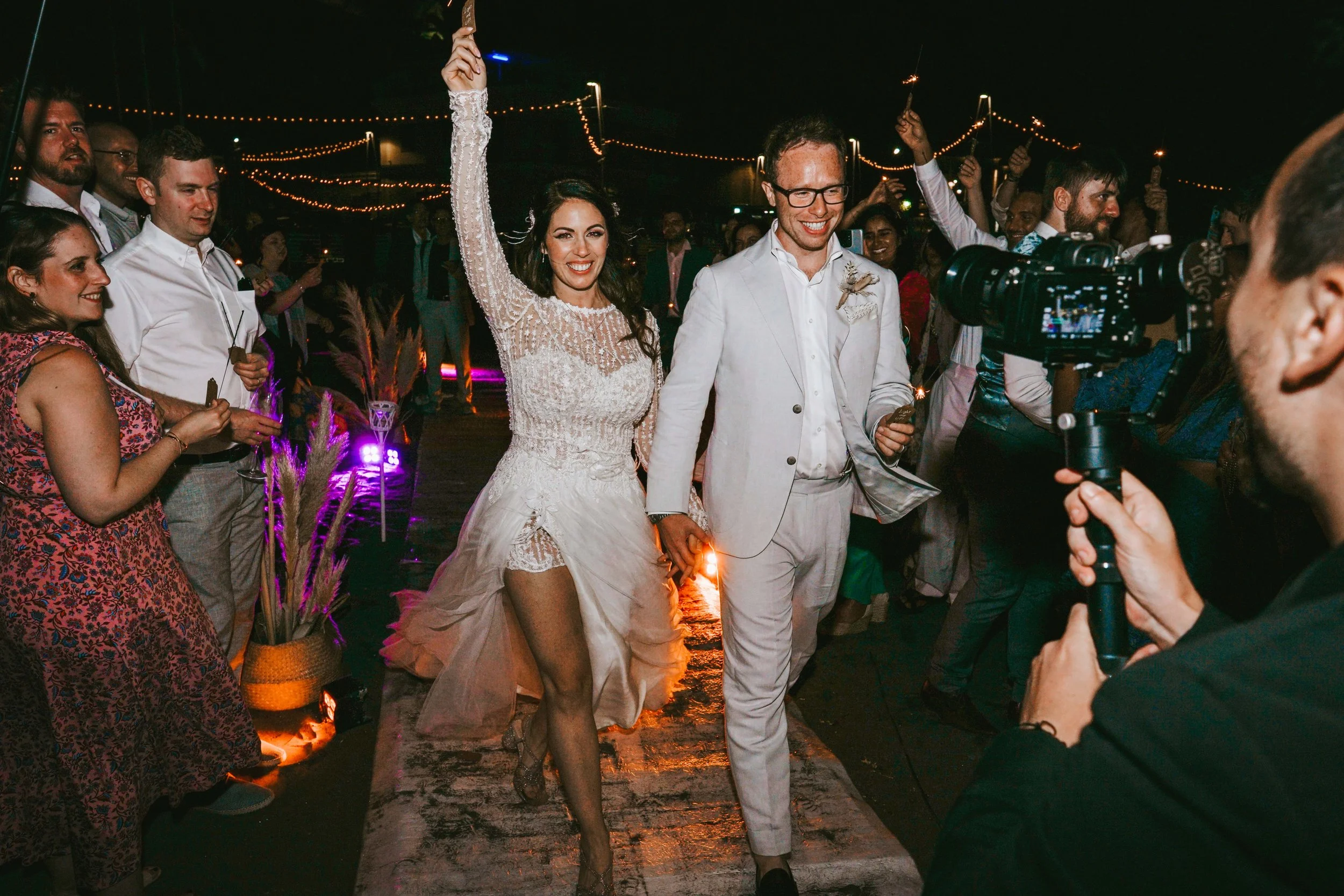 smiling-bride-and-groom-walk-out-onto-beach-on-amalfi-coast-in-italy-with-friends-family-and-sparklers-late-evening-celebrating-with-bucks-wedding-photographer-david-lefebvre.jpg