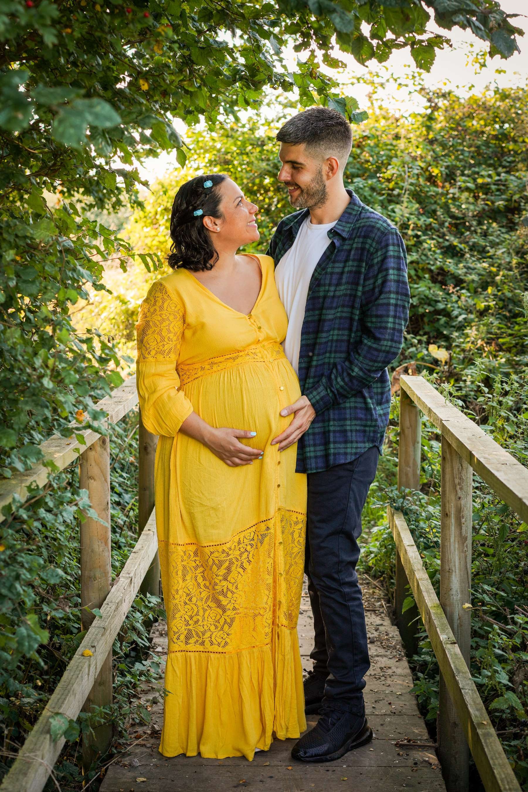 greek-italian-couple-stood-with-bump-on-maternity-boho-shoot-with-photographer-david-lefebvre-on-bridge-in-buckinghamshire--wearing-yellow-dress-and-navy-green-shirt.jpeg