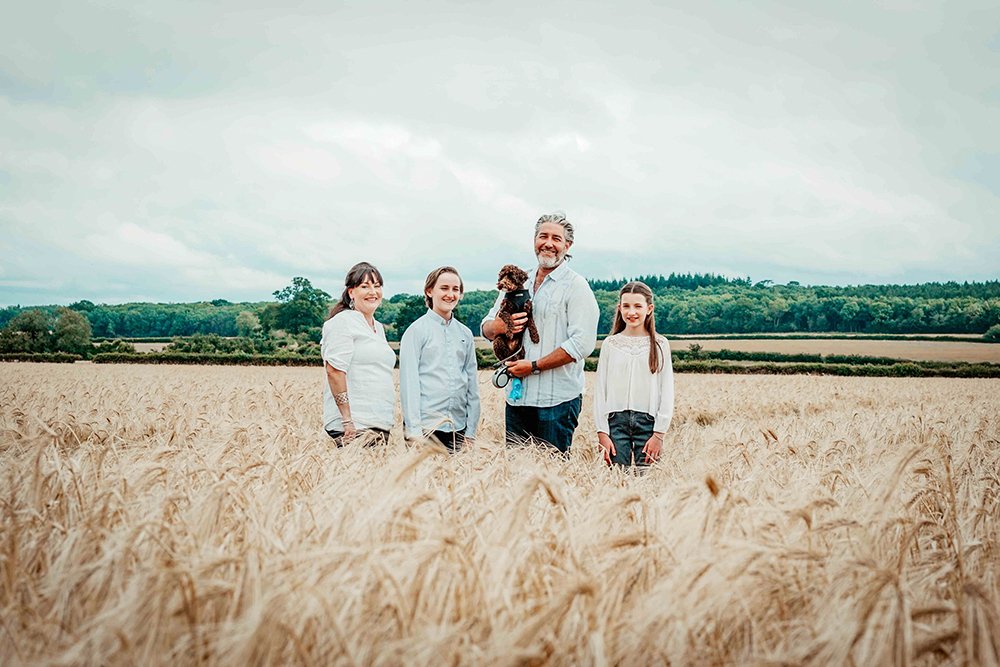 oxfordshire-family-stand-smiling-in-wheat-field-during-day-out-walk-with-dog-near-blenheim-palace-with-david-lefebvre-a-lifestyle-family-photographer-from-buckinghamshire.jpg