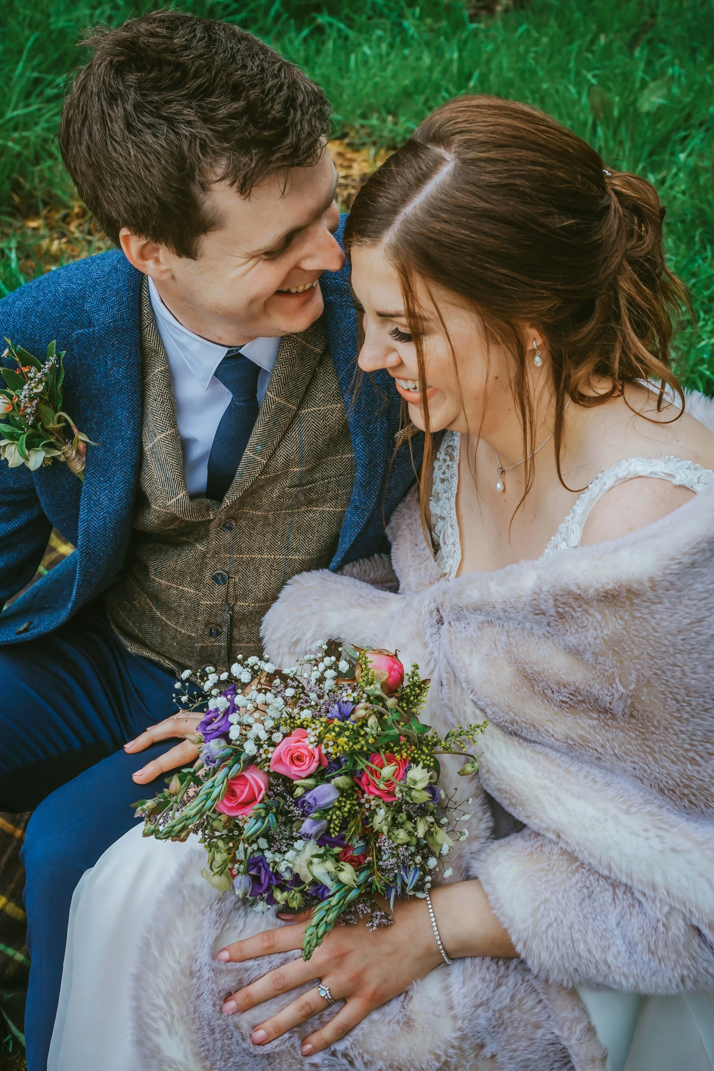 cute-warm-married-couple-sat-close-together-on-log-at-countryside-wedding-wearing-shawl-with-beautiful-wild-flowers-in-buckinghamshire-taken-by-david-lefebvre-photography.jpg