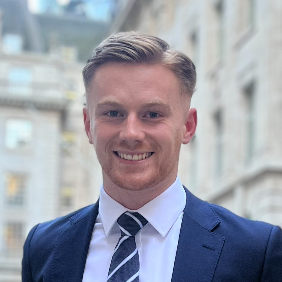 Harrison Carr, Associate at Adam Benedict. Blonde hair styled in loose waves, wearing a black blazer and top, smiling outdoors in an urban setting with vintage buildings of London in the background.