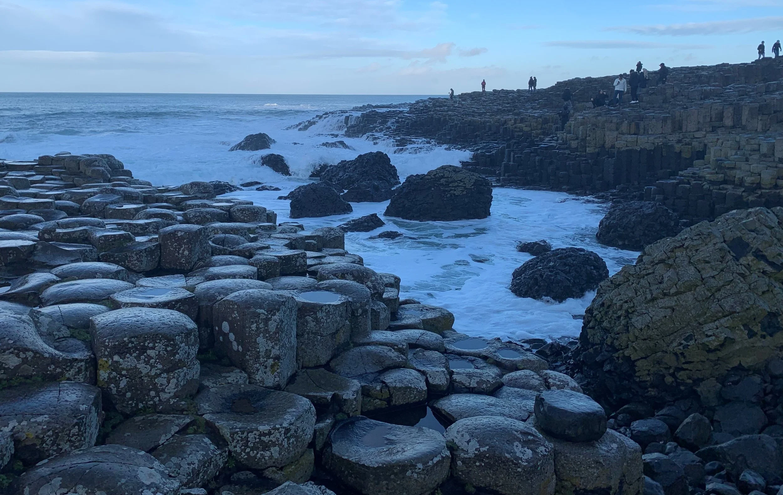 View of the Giant's Causeway, a natural rock formation along the coast with hexagonal basalt columns and visitors exploring the area.