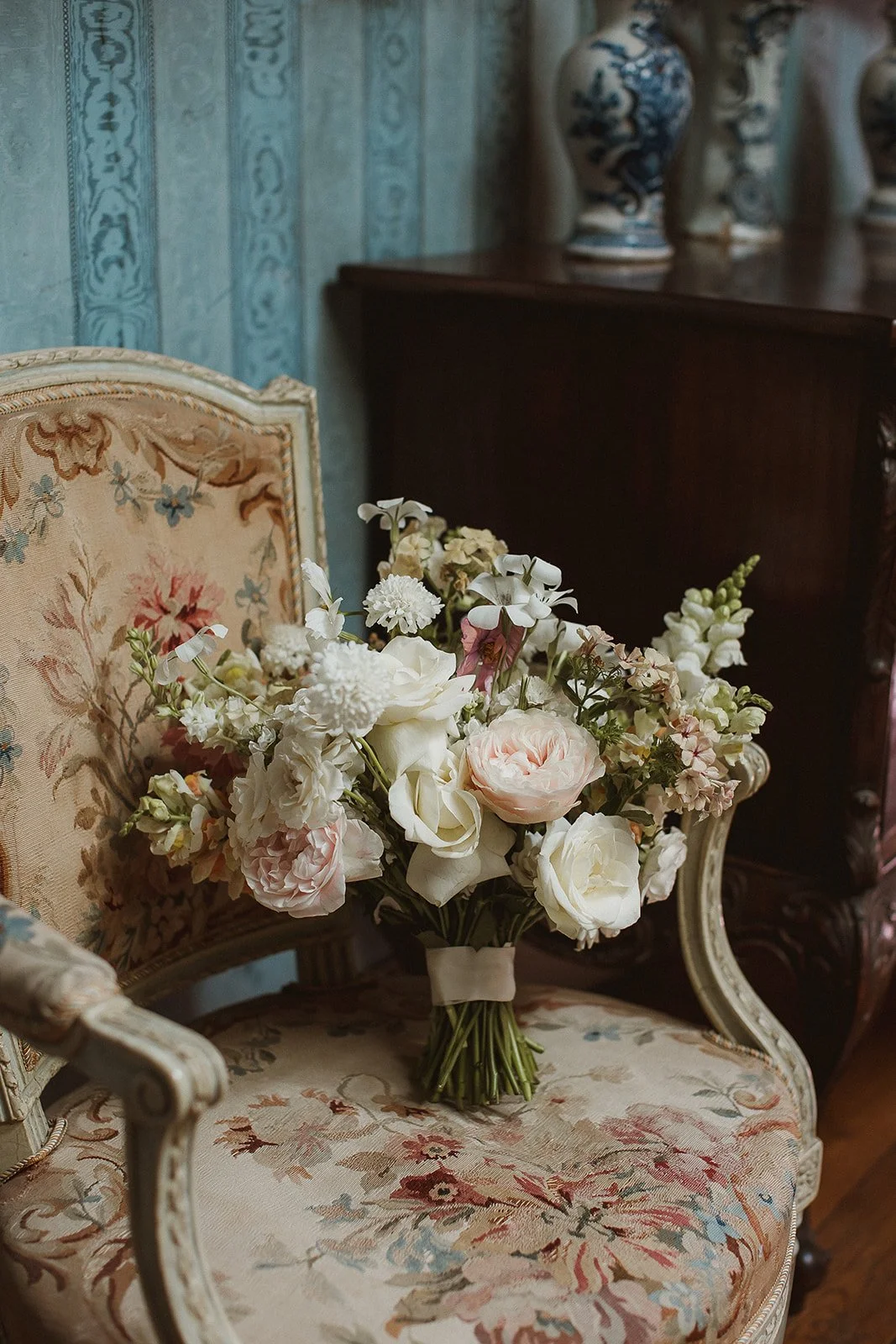 A bouquet of white and pink flowers resting on an antique floral upholstered armchair.