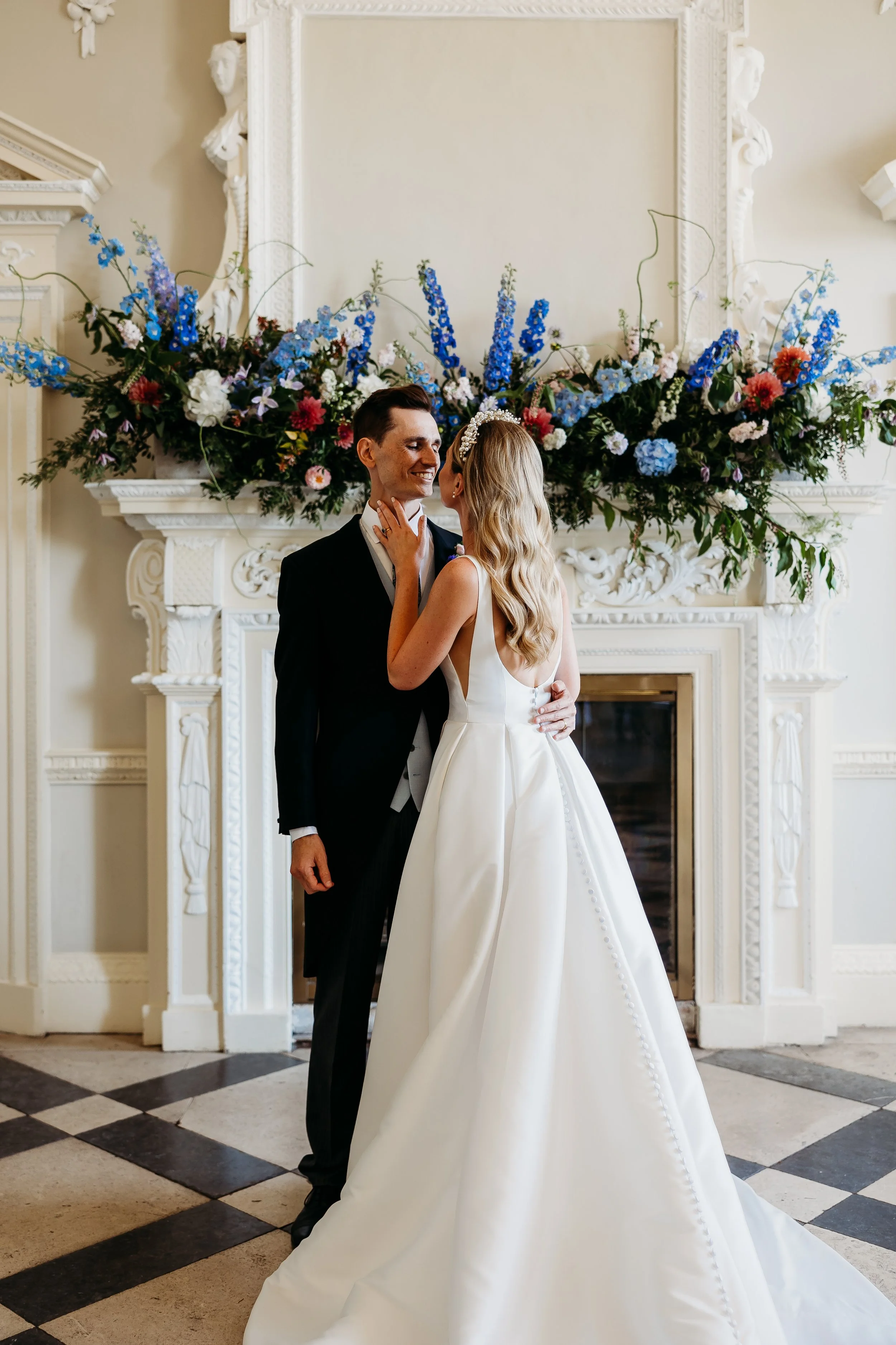 A bride and groom sharing a dance or moment in front of a floral arrangement on a fireplace in a wedding venue.