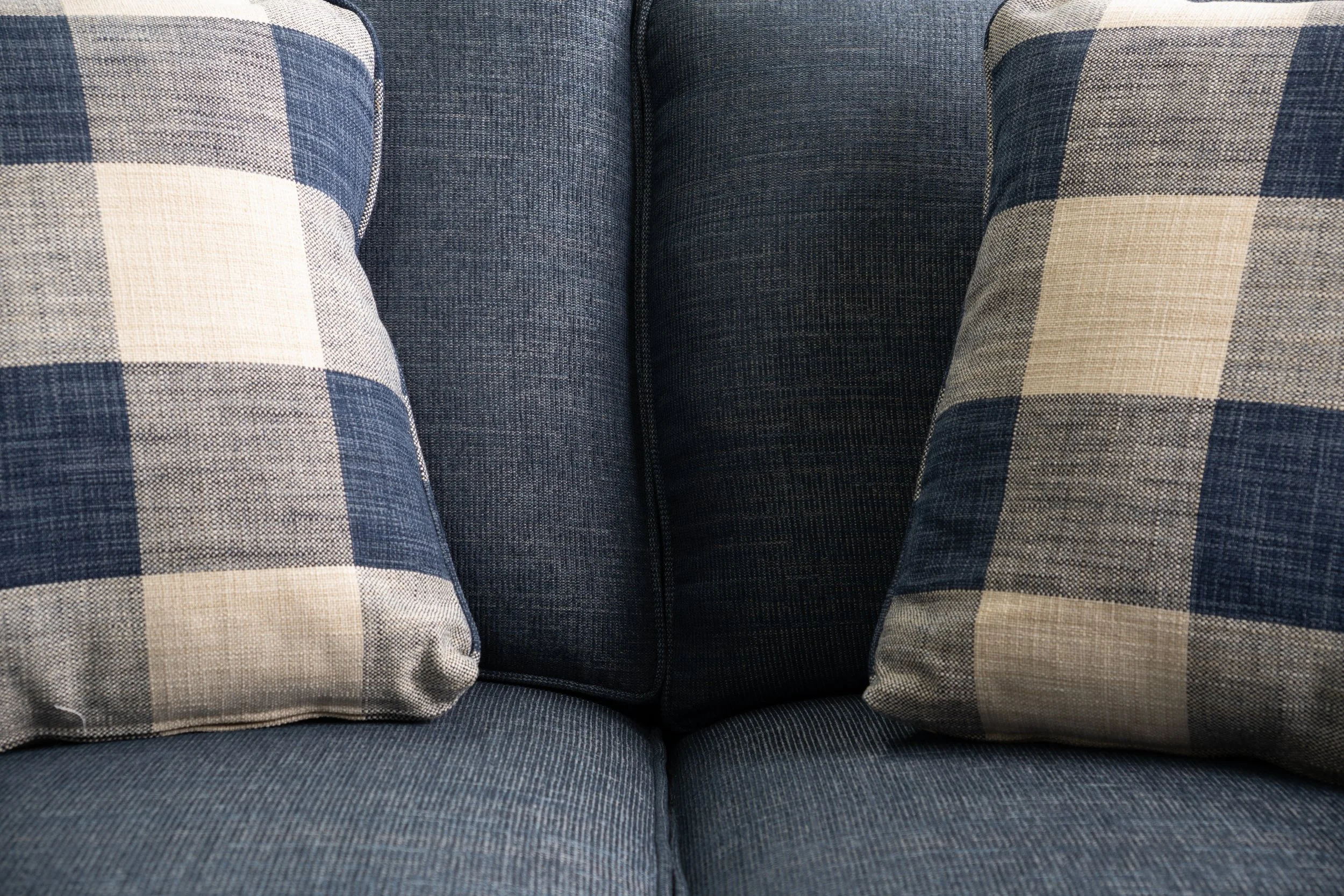 Close-up of a blue fabric sofa with two plaid-patterned pillows on each side.