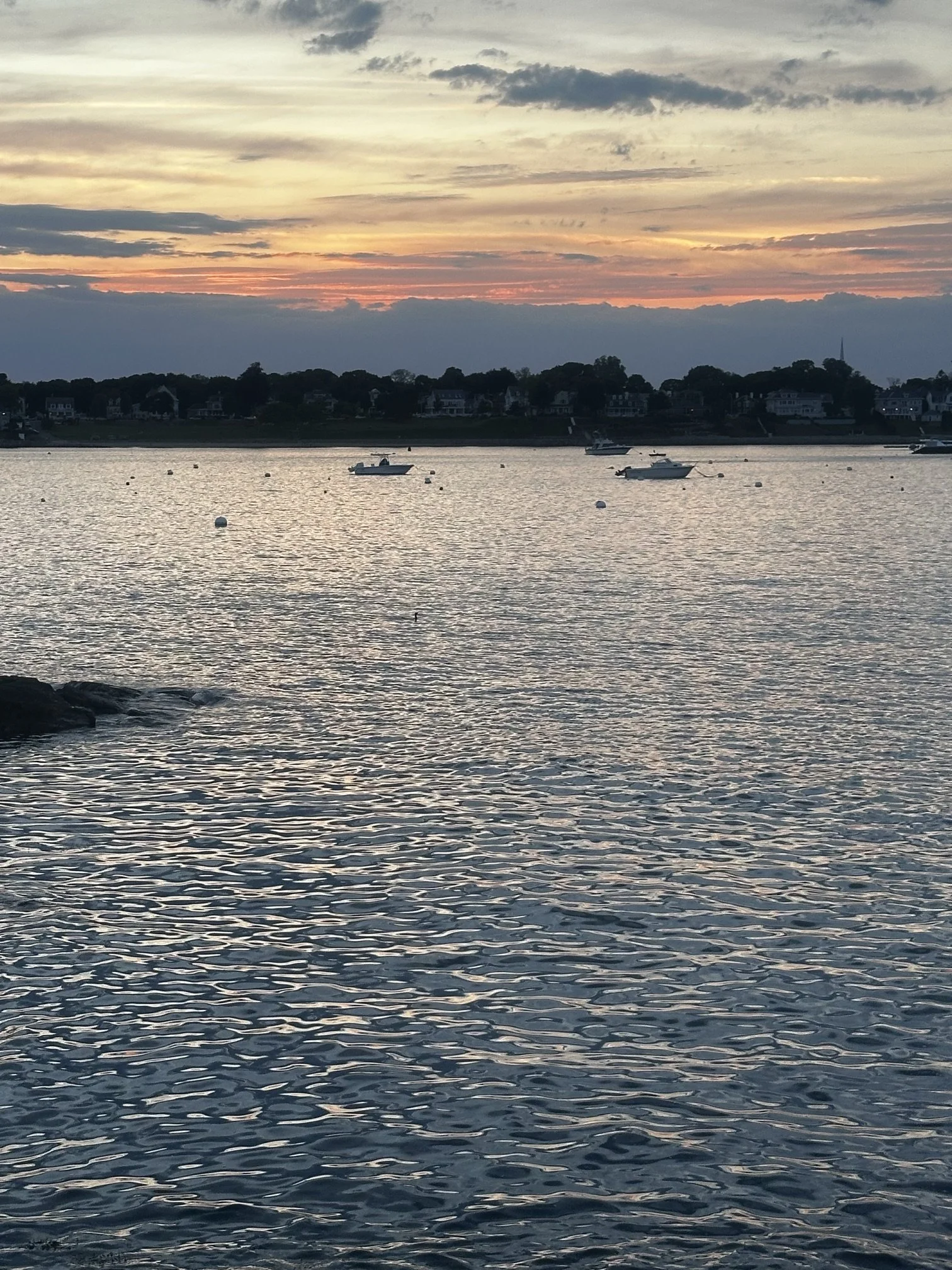 A sunset over a body of water with boats and houses in the distance