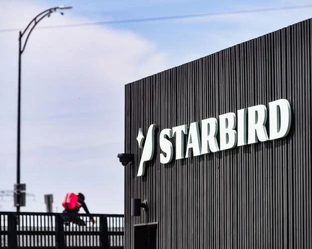 Close-up of a black building with the 'STARBIRD' logo and sign, and a person walking on the sidewalk nearby.