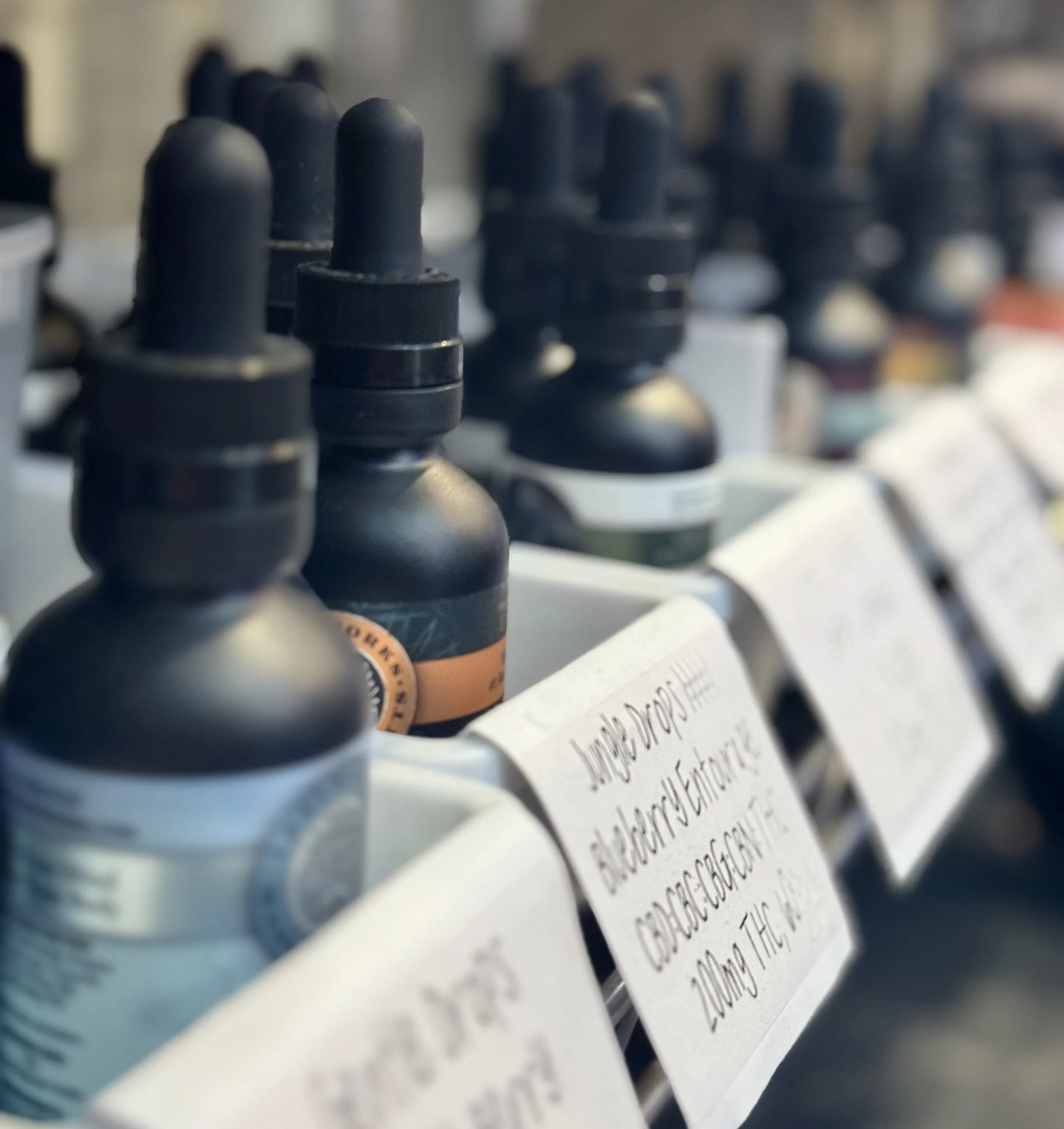 Several small black bottles with droppers on store shelves, section labeled with handwritten signs.