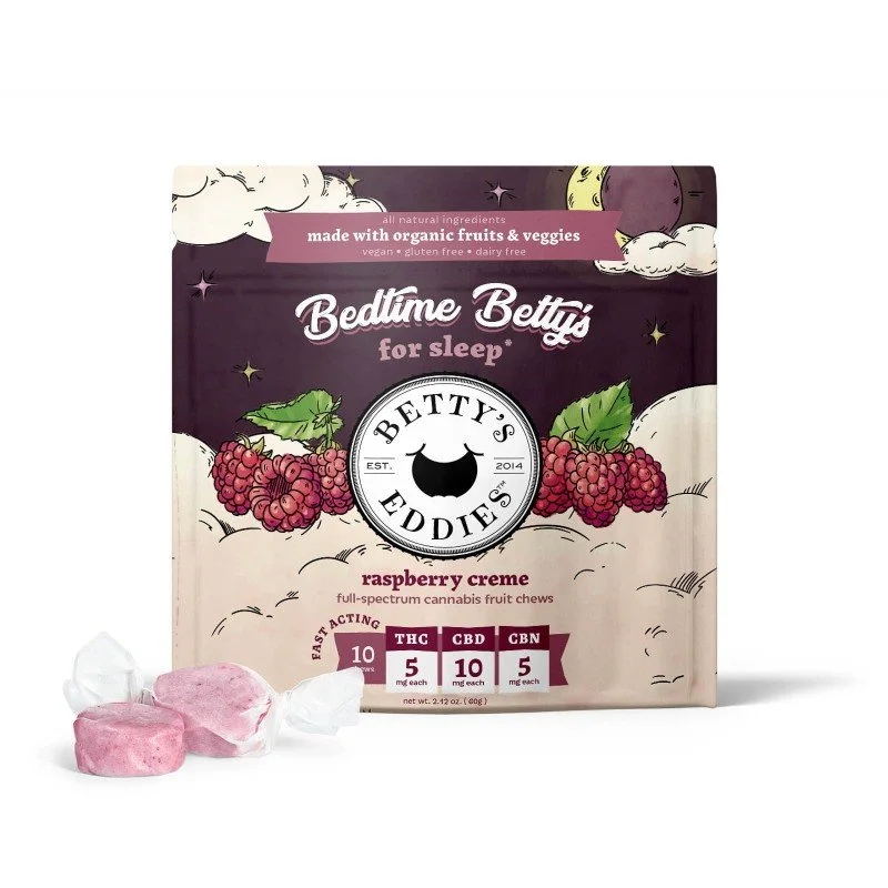 Betty's Eddies bedtime Betty's raspberry crème cannabis fruit chews in a purple and white package with raspberries and clouds, and three pink chews with white wrappers in front.