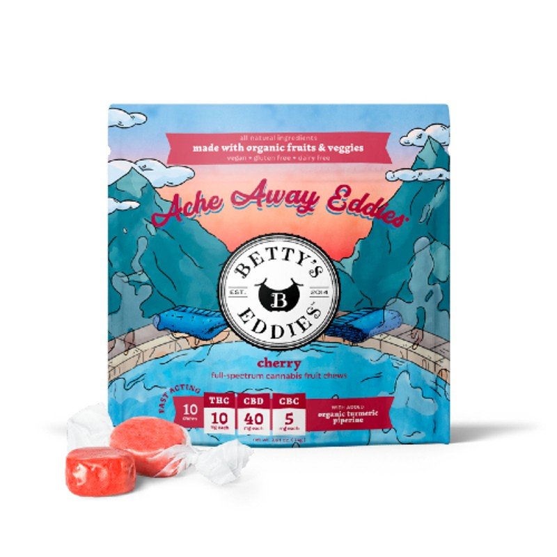 Packaging of Betty's Eddie's Ache Away Eddies cherry cannabis fruit chews, with a graphic illustration of mountains, clouds, and a pond, and a couple of chews in front.