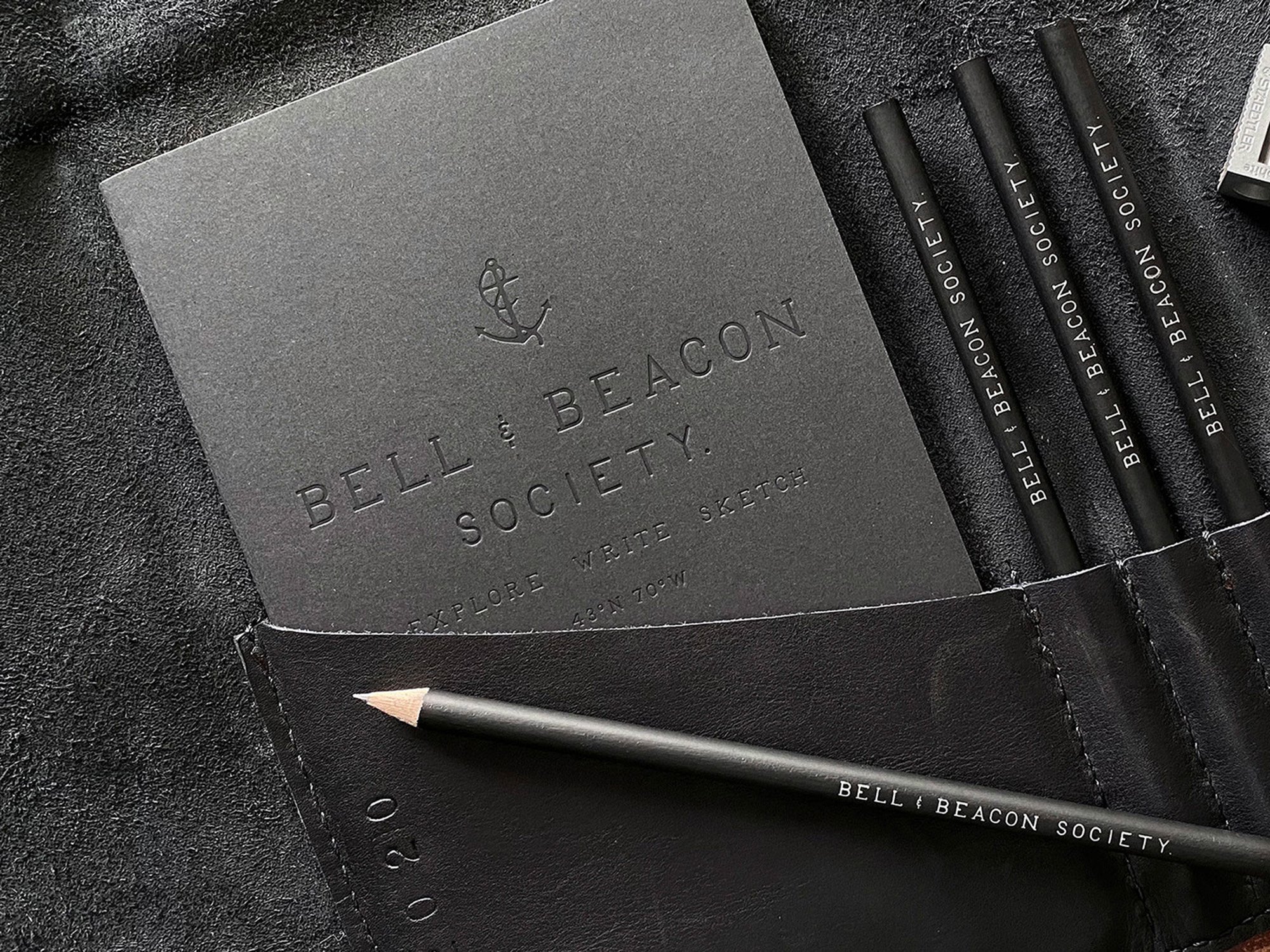 Bell & Beacon Society brand identity stationery with embossed logo, pencils, and black paper materials designed by Murphy Empire.