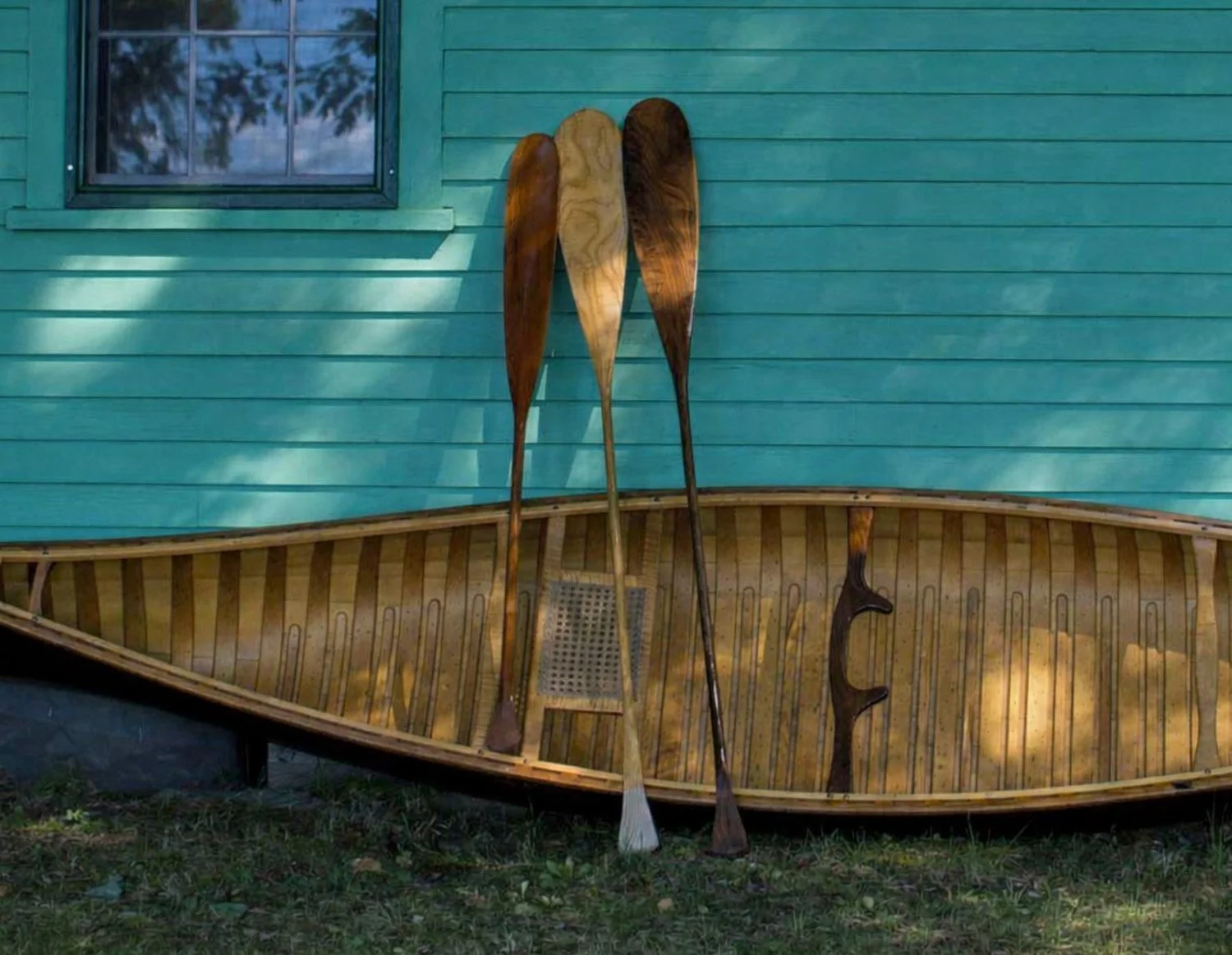 Handcrafted wooden canoe with Shaw & Tenney paddles against teal wall, Maine heritage craftsmanship