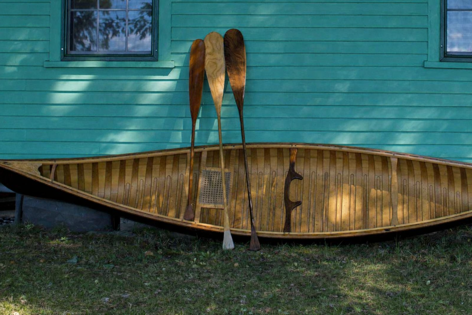 Handcrafted wooden canoe with Shaw & Tenney paddles against teal wall, Maine heritage craftsmanship